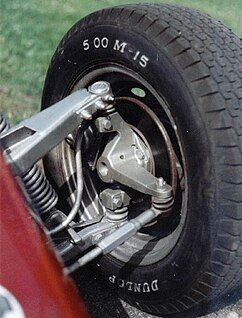Close-up of a car wheel and suspension assembly, with a black tire mounted on a red vehicle.