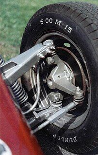 Close-up of a car wheel and suspension assembly, with a black tire mounted on a red vehicle.