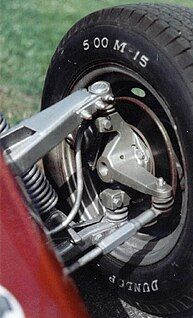 Close-up of a car wheel and suspension assembly, with a black tire mounted on a red vehicle.