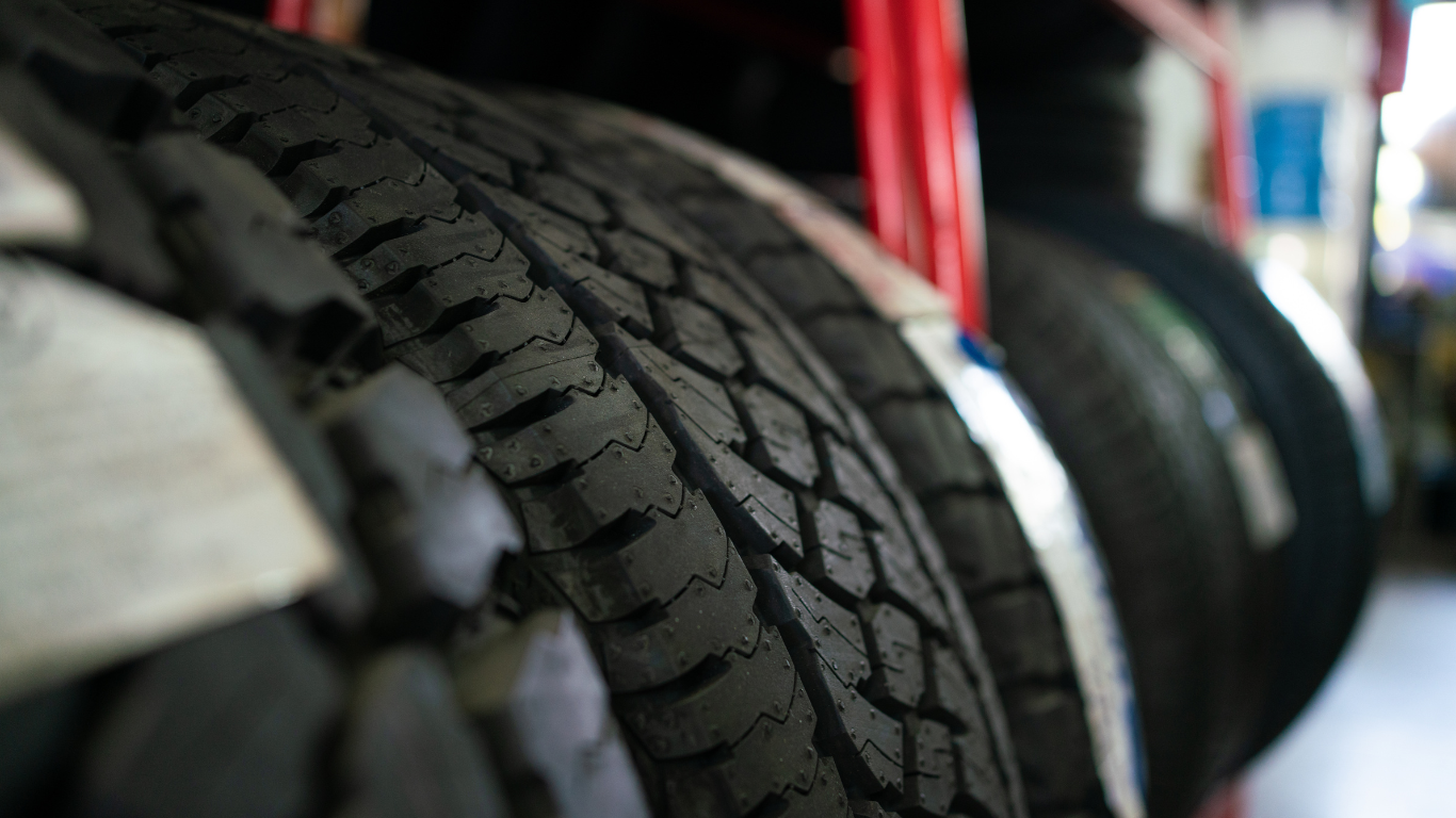 Close-up view of a row of black tires with tread patterns stored on a rack, likely at a tire shop.