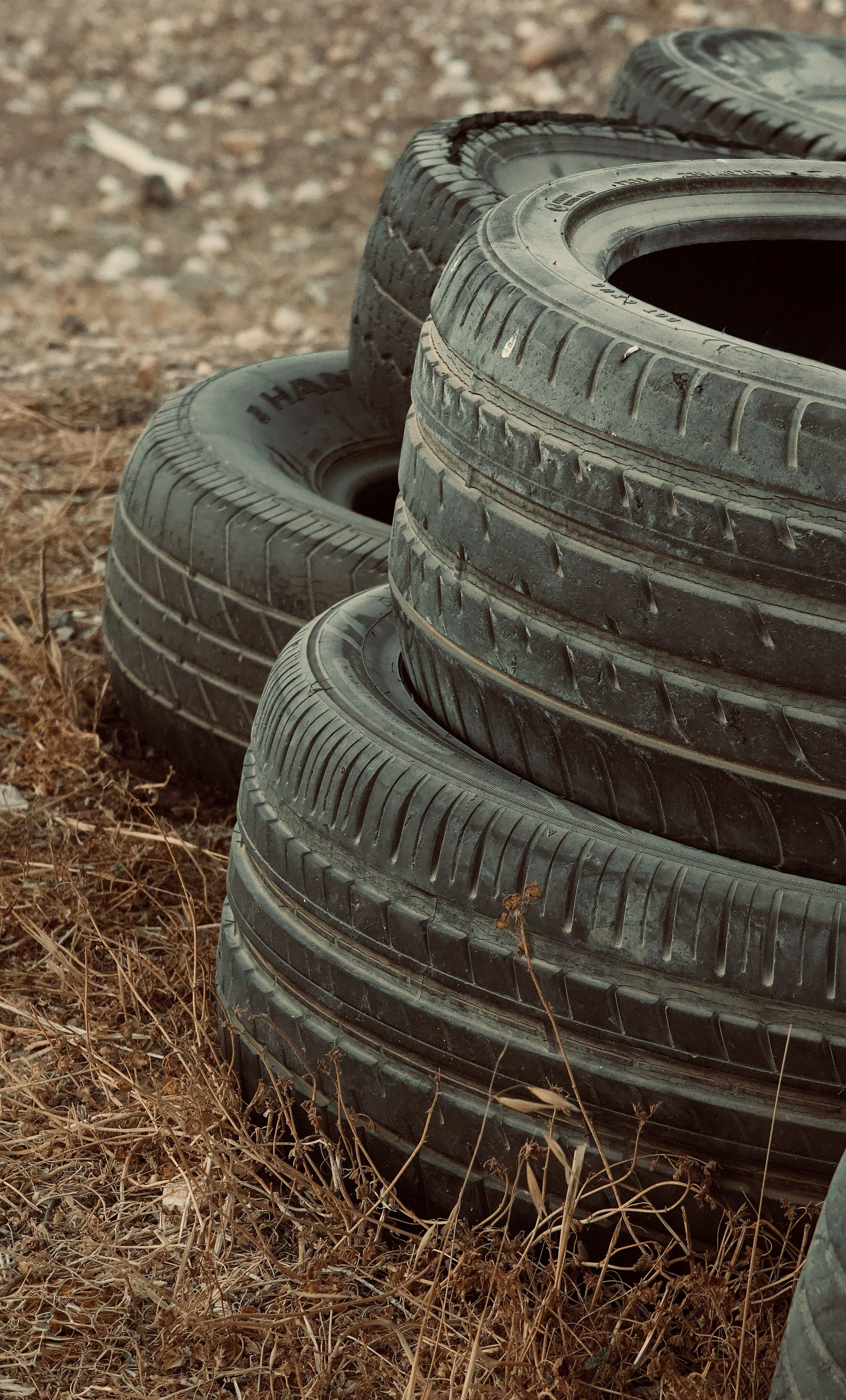 Stacked black tires on a dirt surface with dry grass around them