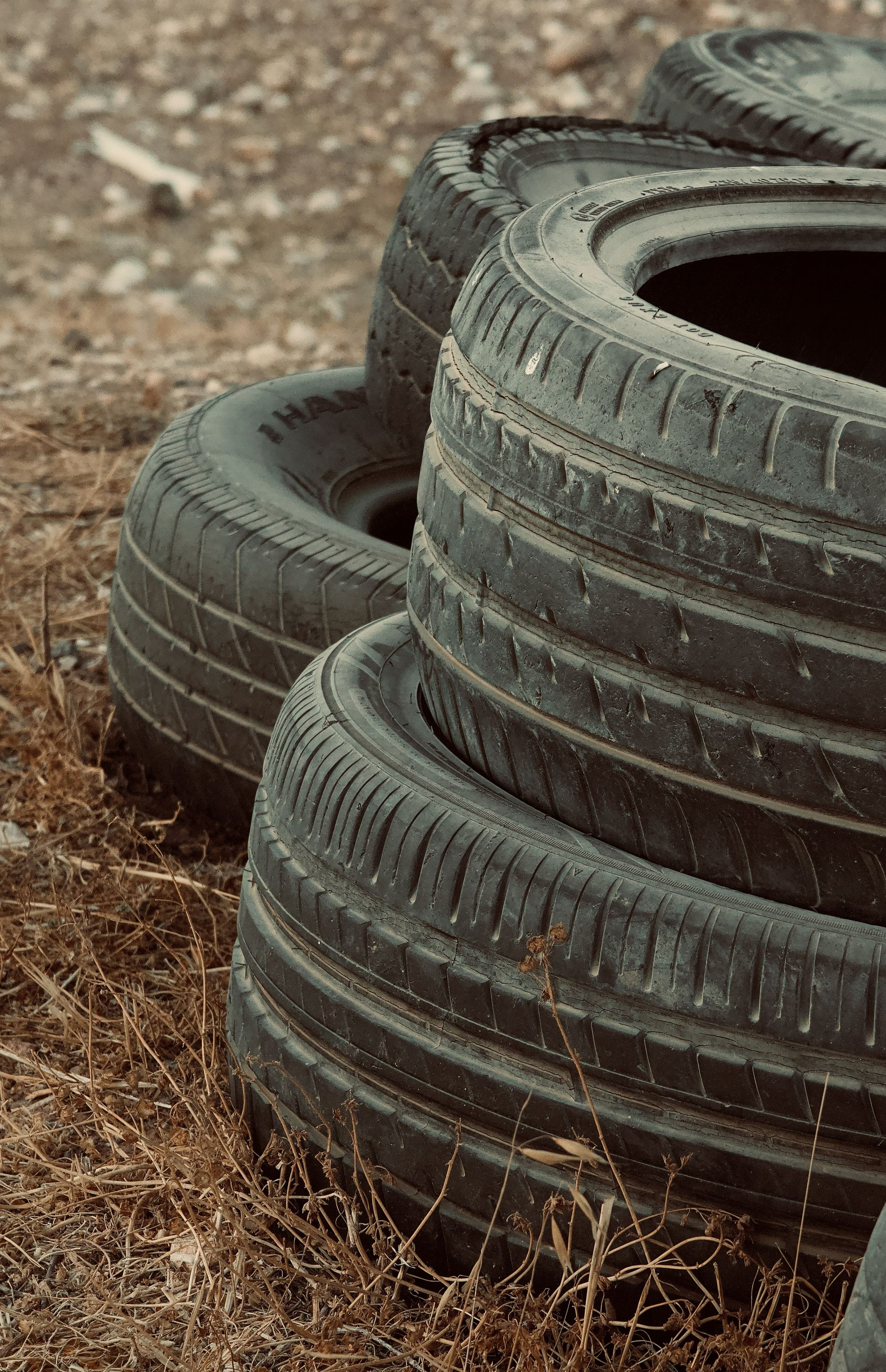 Stacked black tires on a dirt surface with dry grass around them