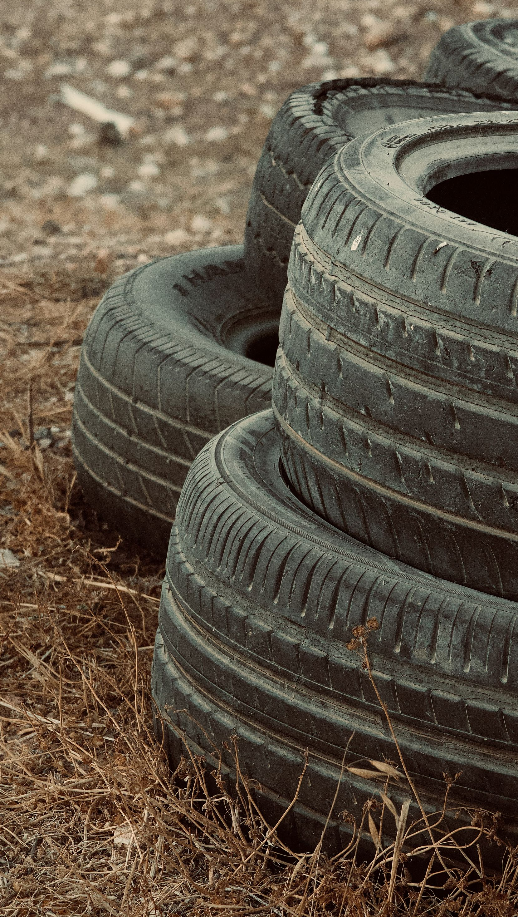 Stacked black tires on a dirt surface with dry grass around them