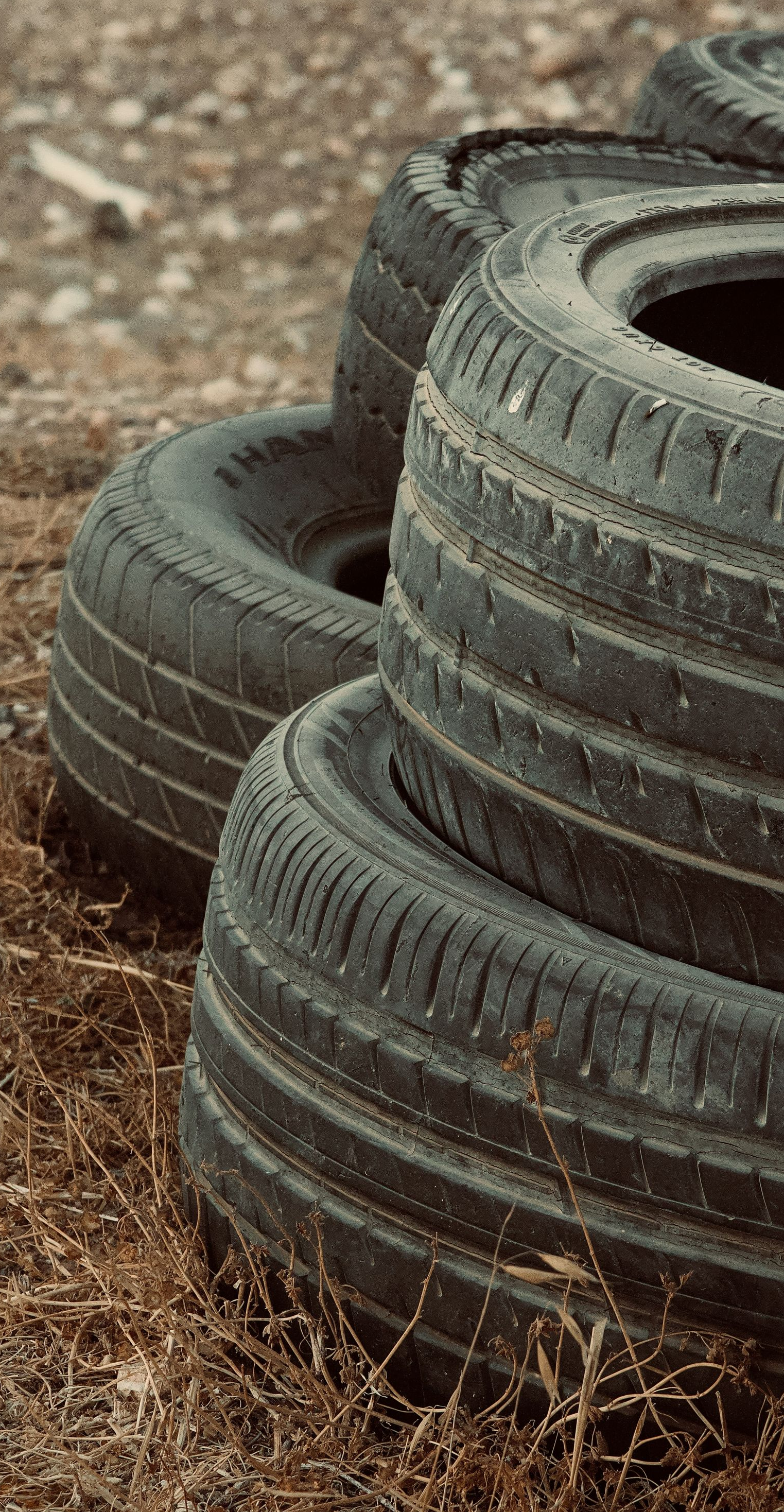 Stacked black tires on a dirt surface with dry grass around them