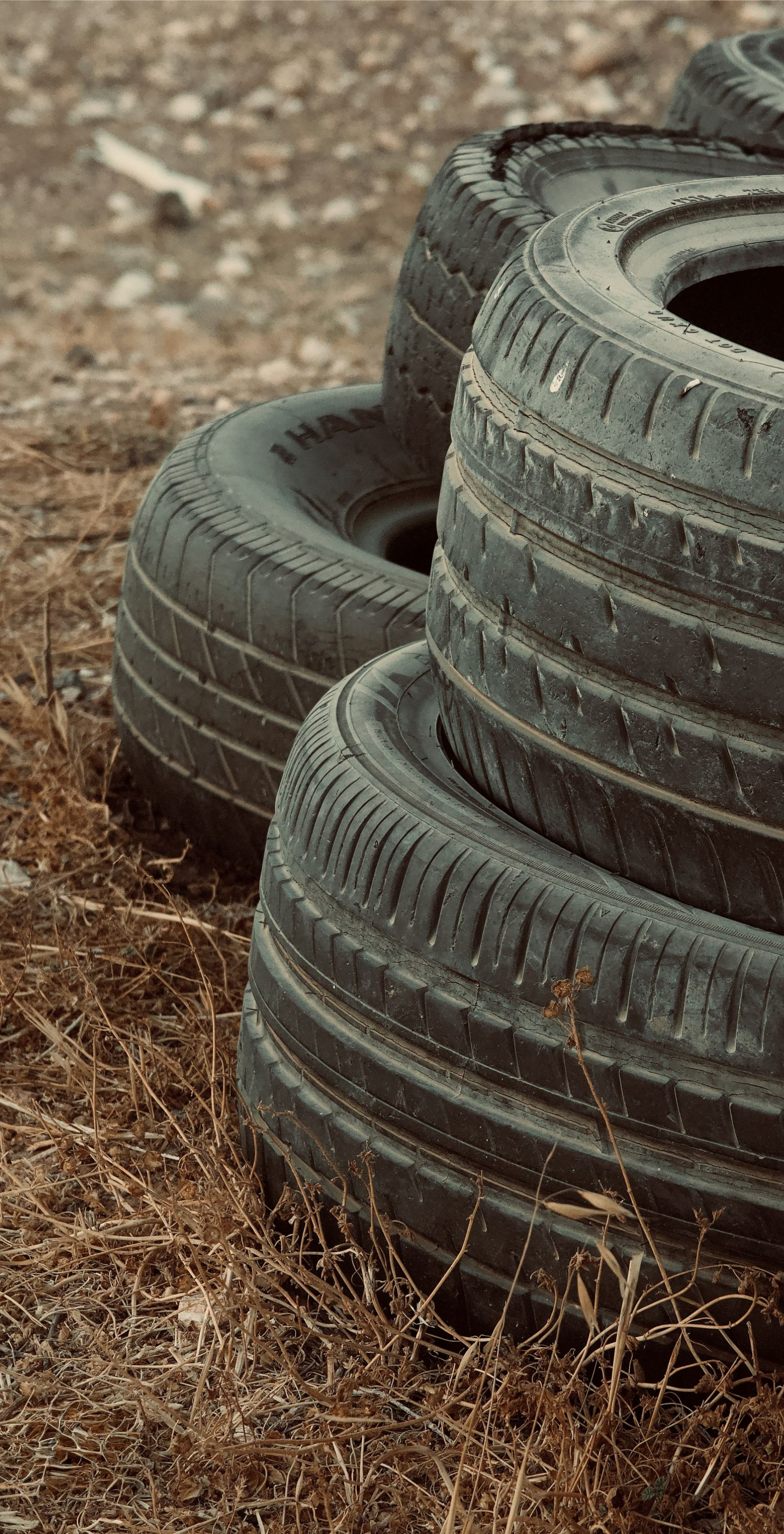 Stacked black tires on a dirt surface with dry grass around them