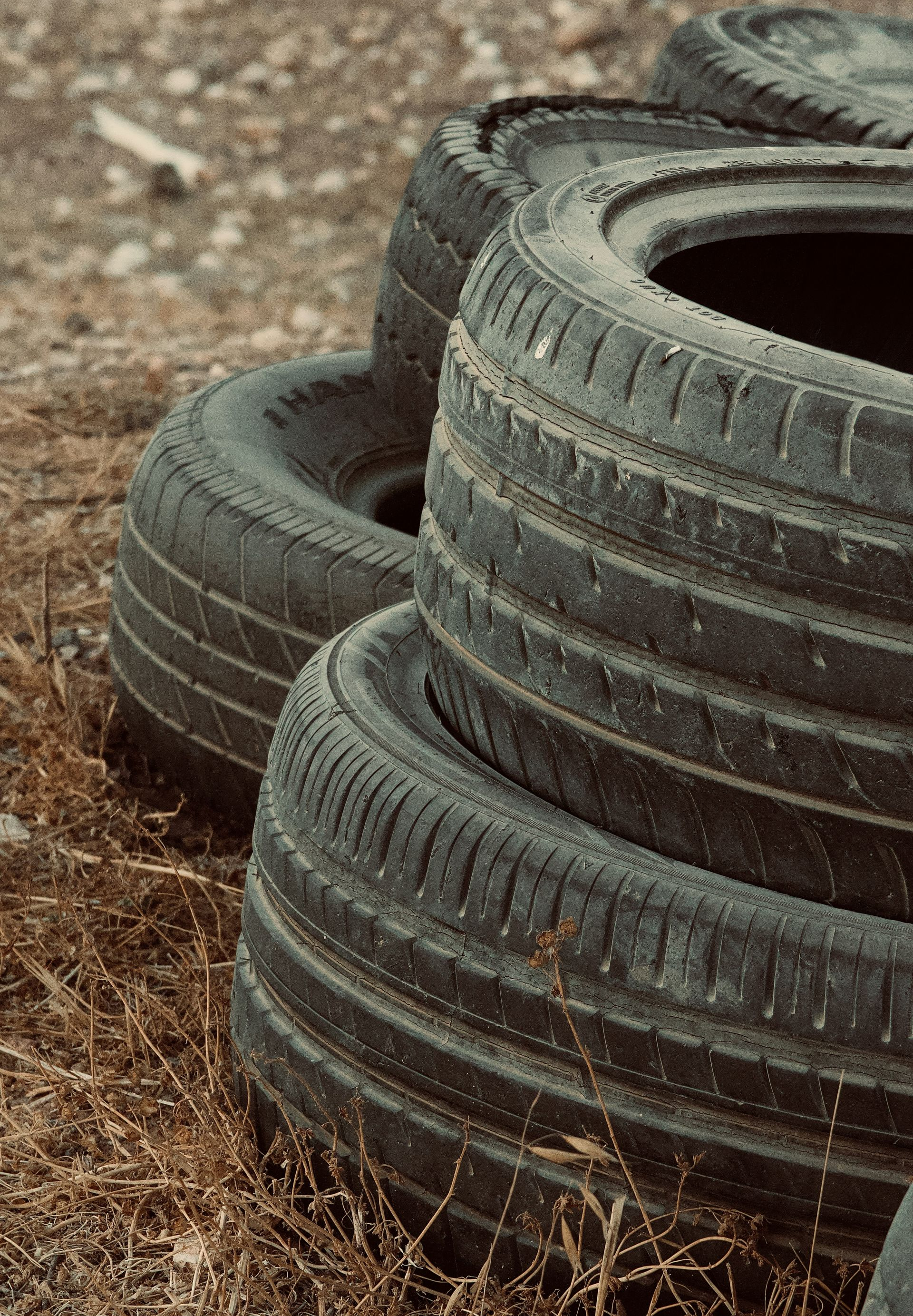 Stacked black tires on a dirt surface with dry grass around them