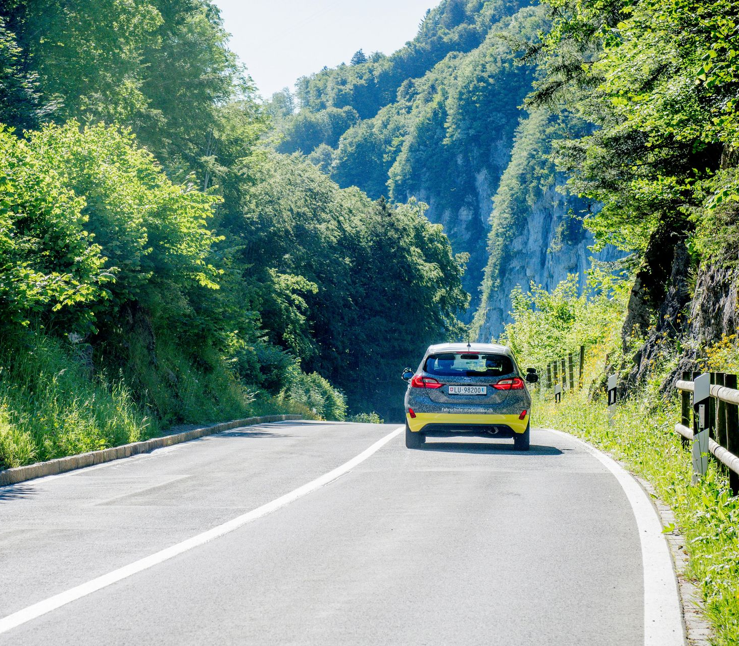 Car driving on a curving mountain road beside lush green trees and hills