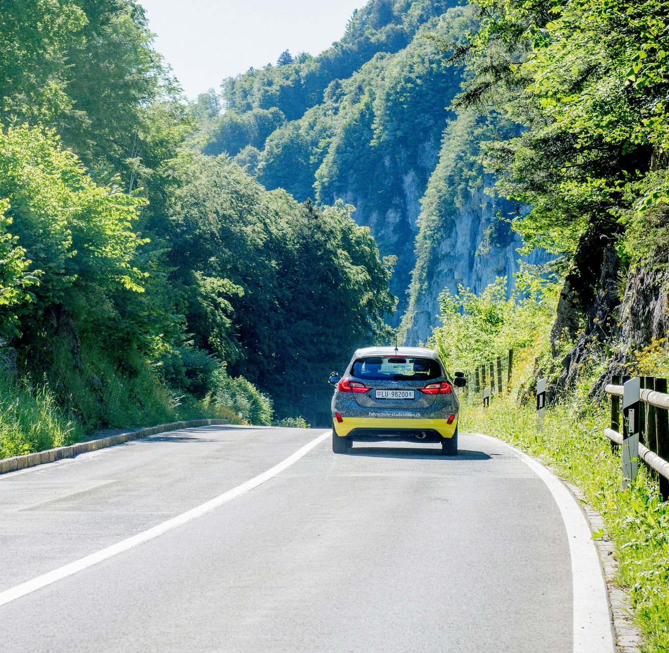 Car driving on a curving mountain road beside lush green trees and hills