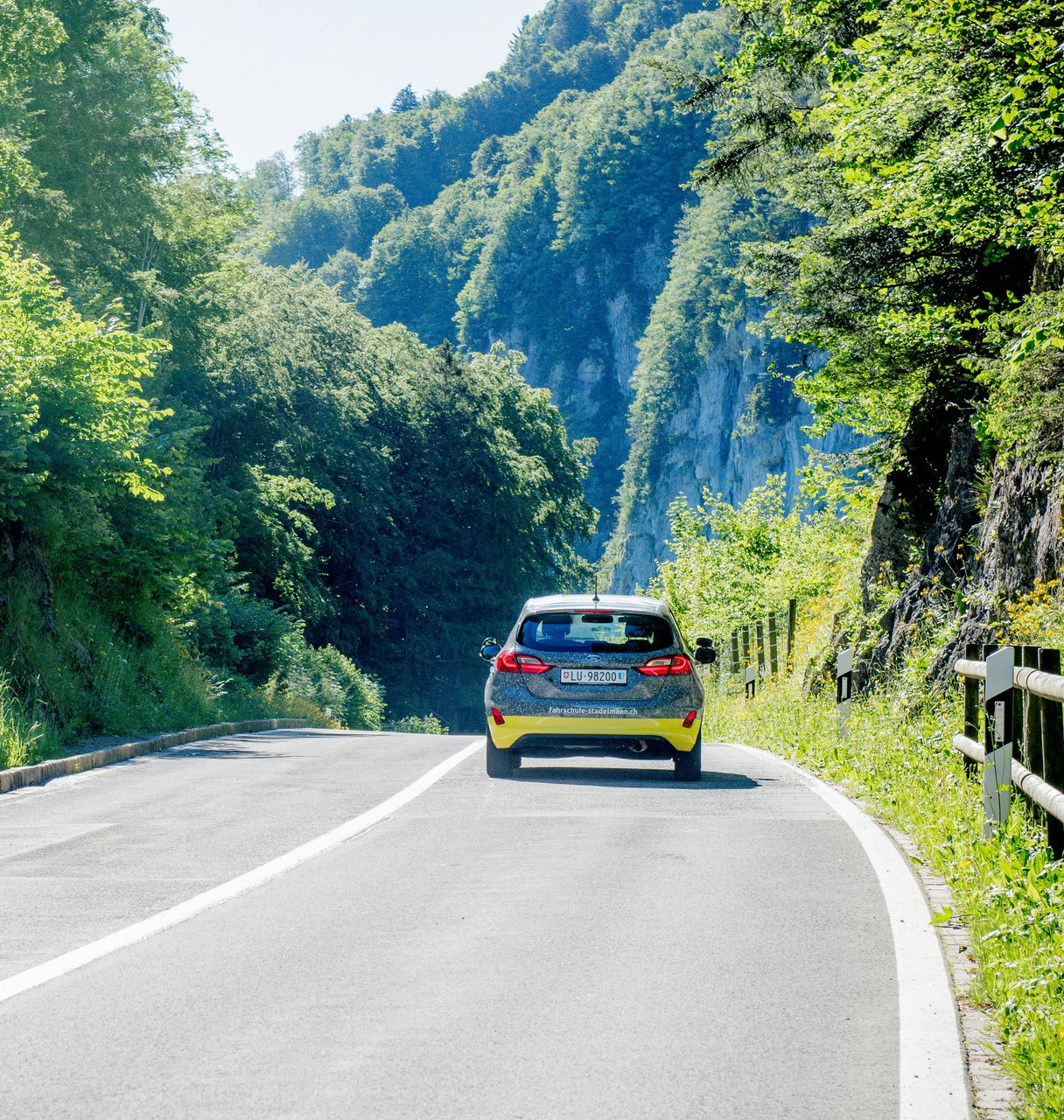 Car driving on a curving mountain road beside lush green trees and hills