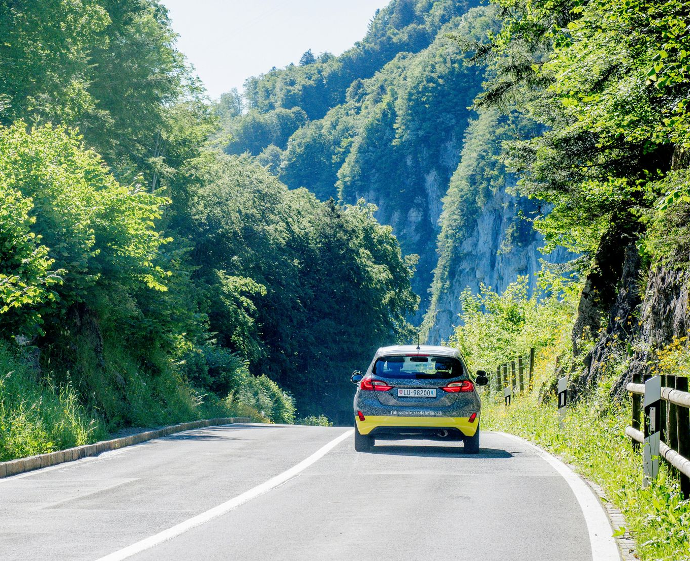 Car driving on a curving mountain road beside lush green trees and hills