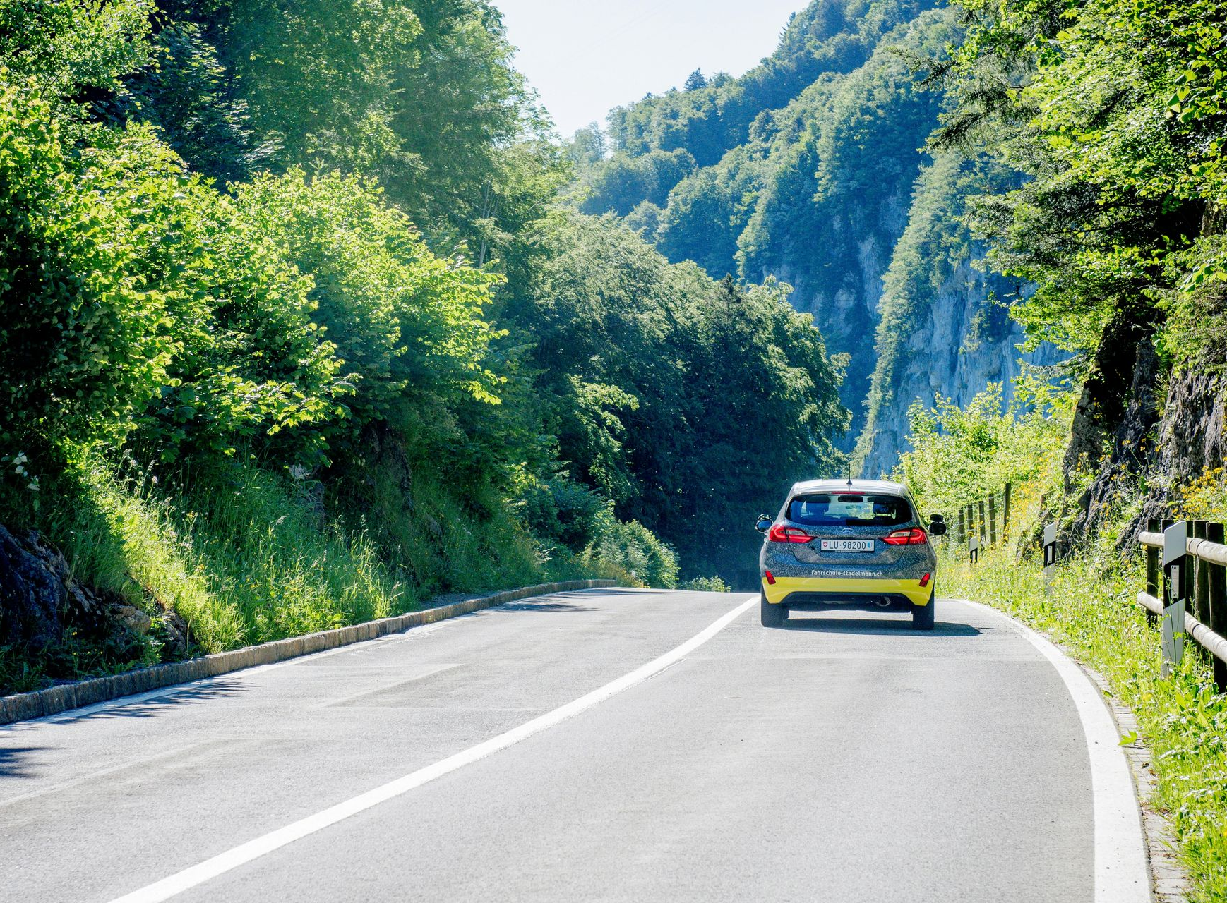 Car driving on a curving mountain road beside lush green trees and hills