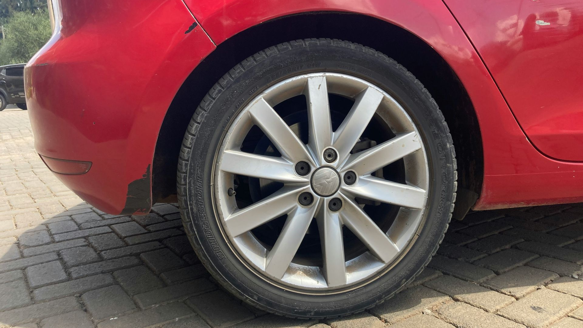 Rear side of a red car, showing the wheel and tire parked on a paved surface
