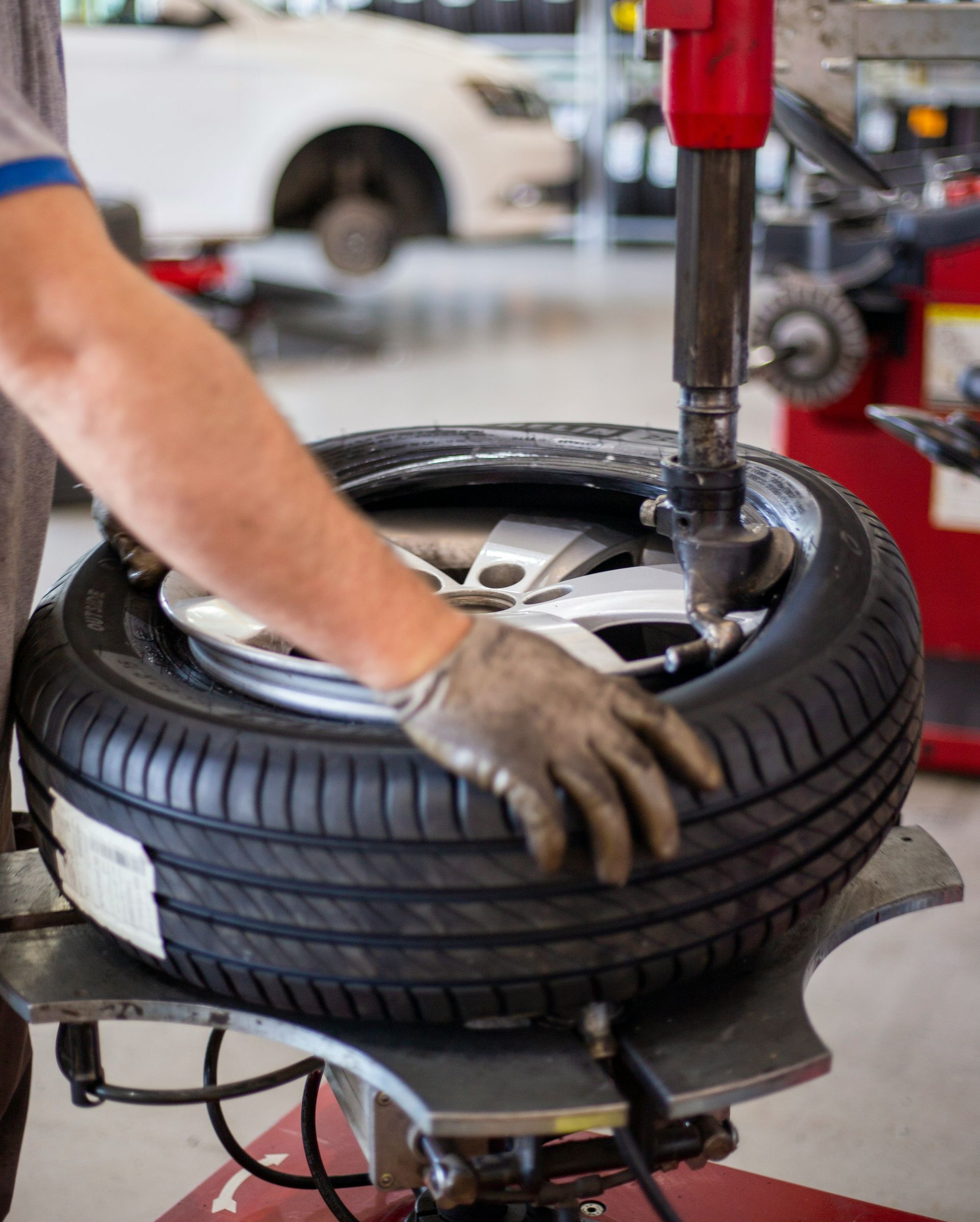 A technician wearing a glove uses a tire changing machine to mount a tire onto a car wheel in a workshop.