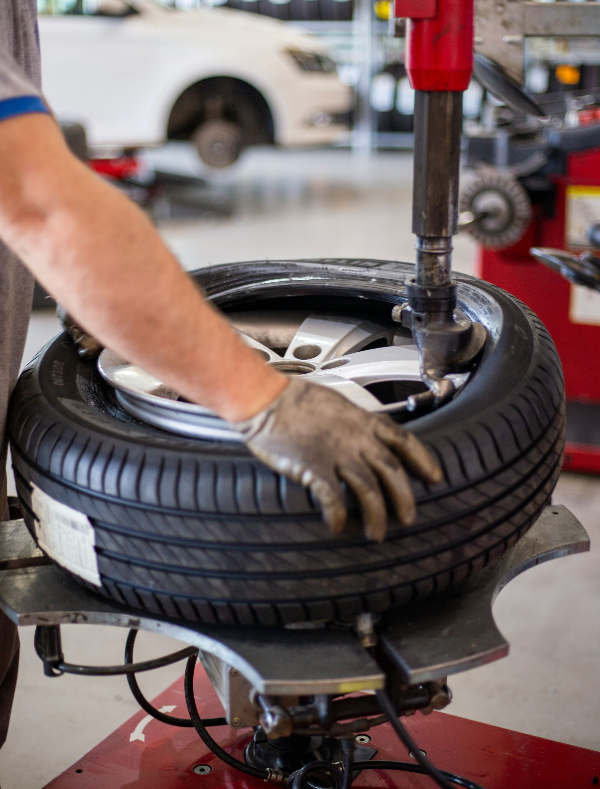 A technician wearing a glove uses a tire changing machine to mount a tire onto a car wheel in a workshop.