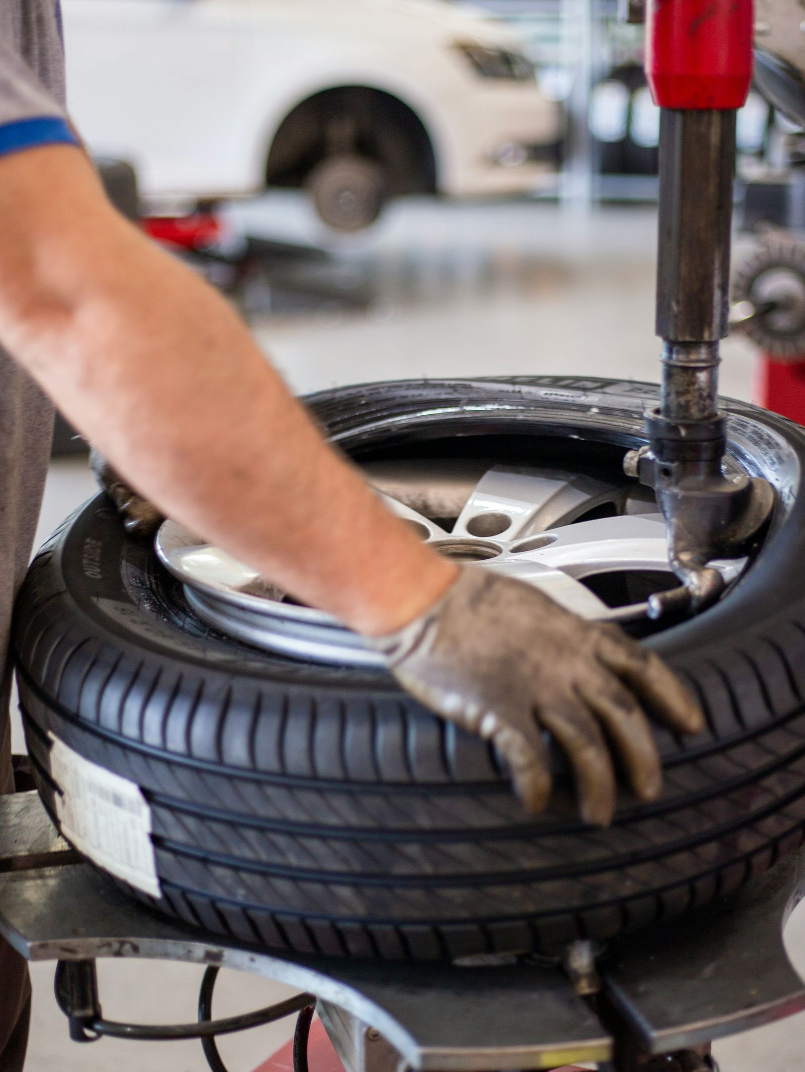 A technician wearing a glove uses a tire changing machine to mount a tire onto a car wheel in a workshop.