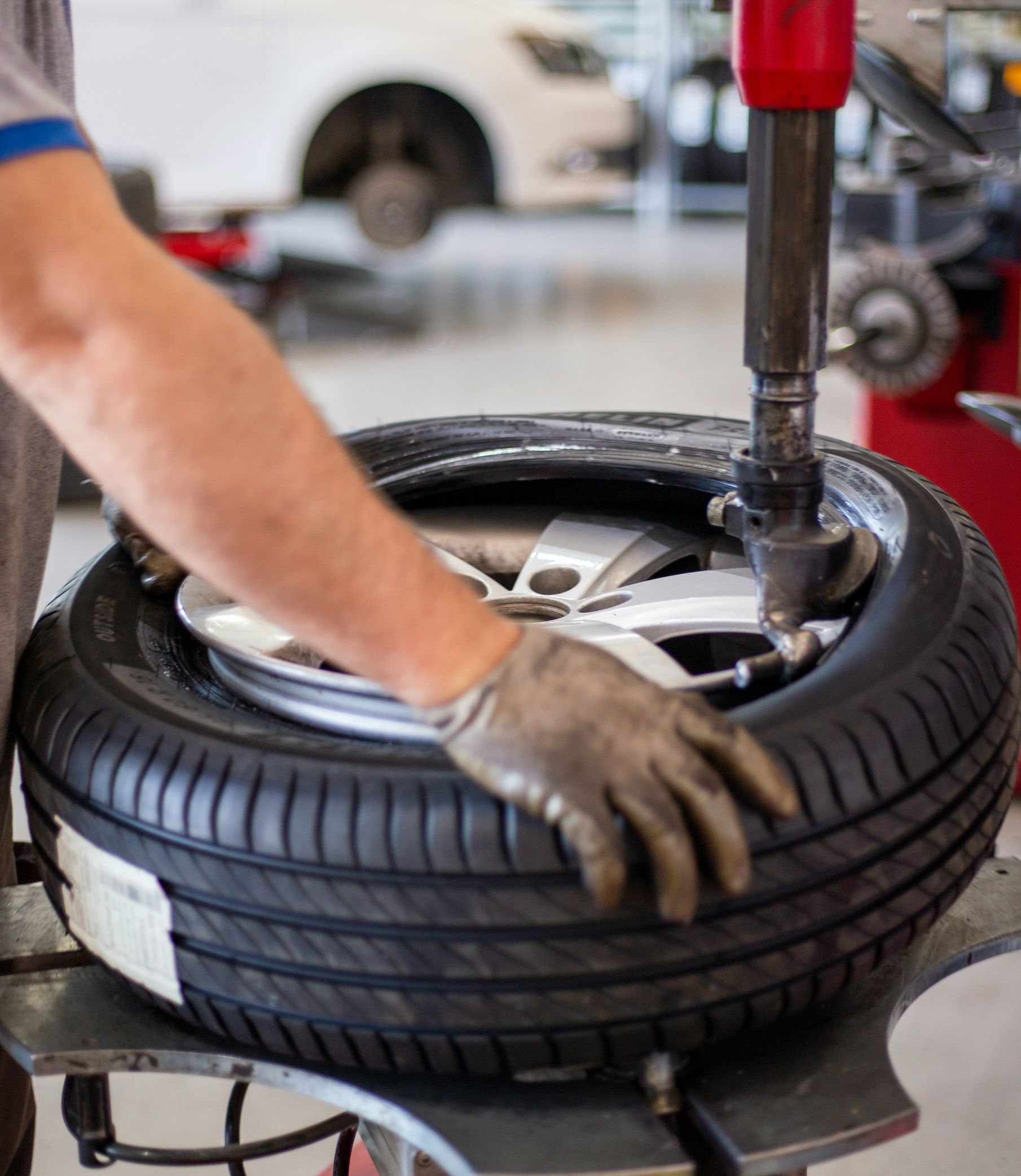 A technician wearing a glove uses a tire changing machine to mount a tire onto a car wheel in a workshop.