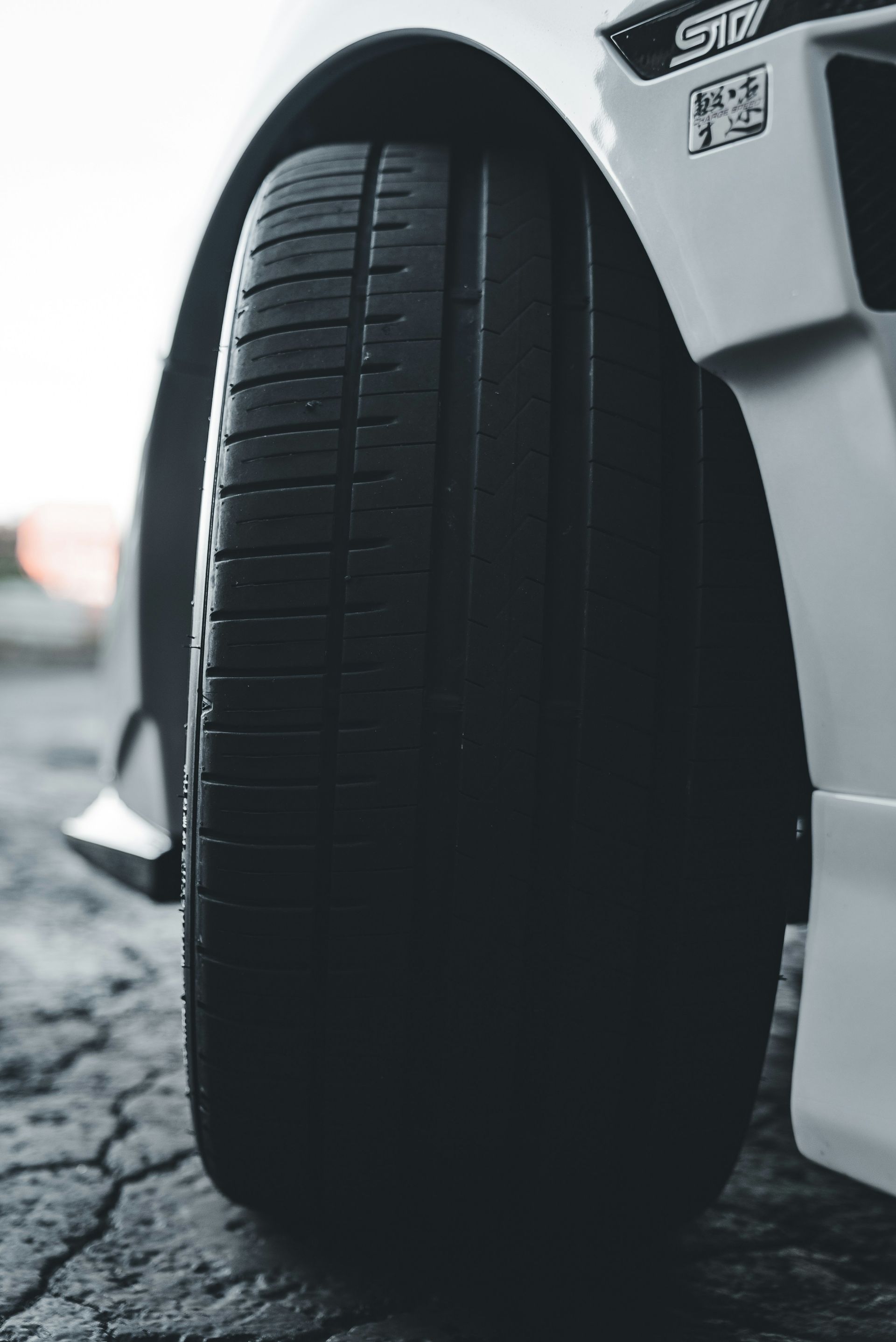 Close-up of a car tire beside a white vehicle on a wet road.