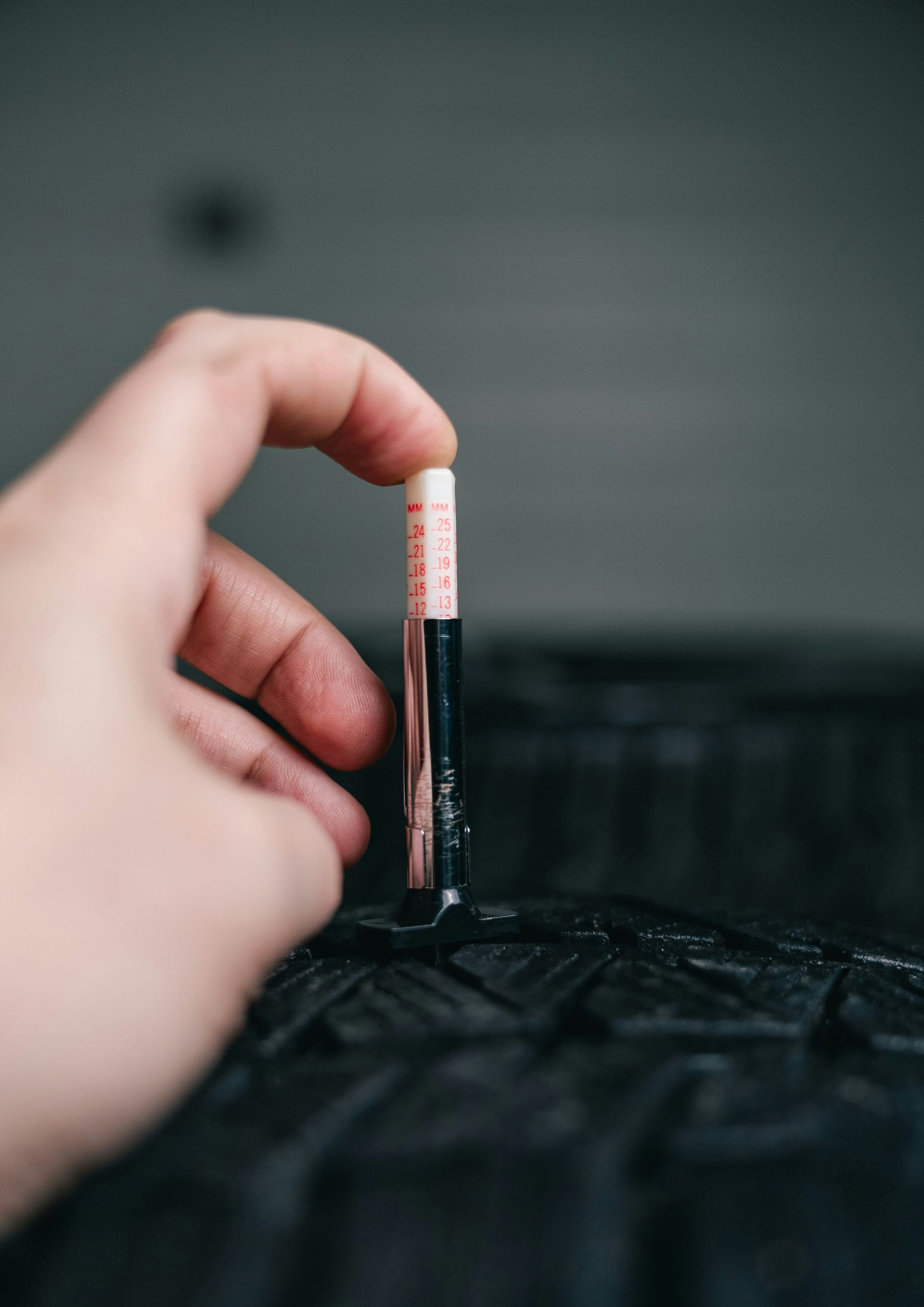Person using a tire tread depth gauge to measure tire wear.