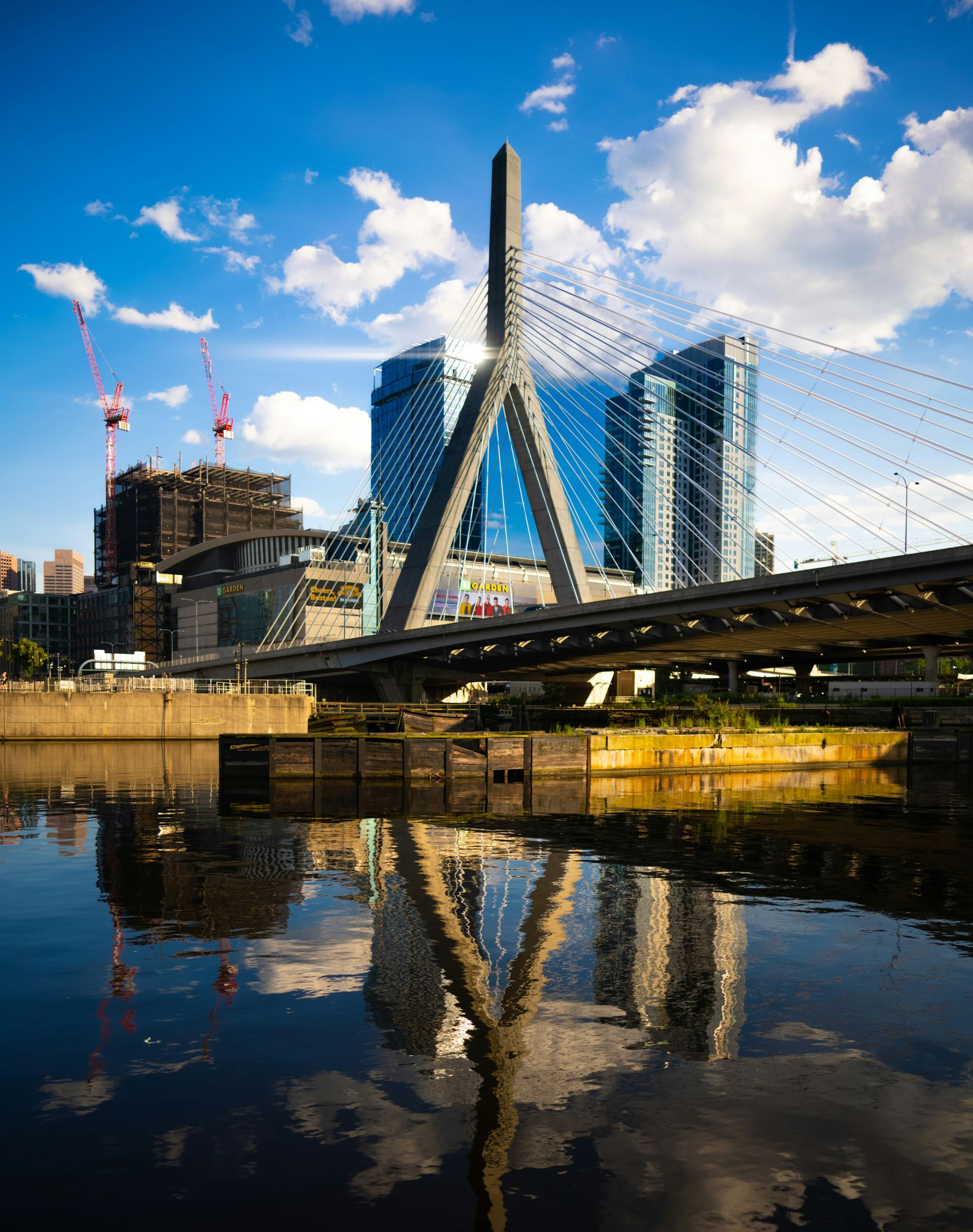 The Leonard P. Zakim Bunker Hill Memorial Bridge reflected in the Charles River under a blue sky with clouds.