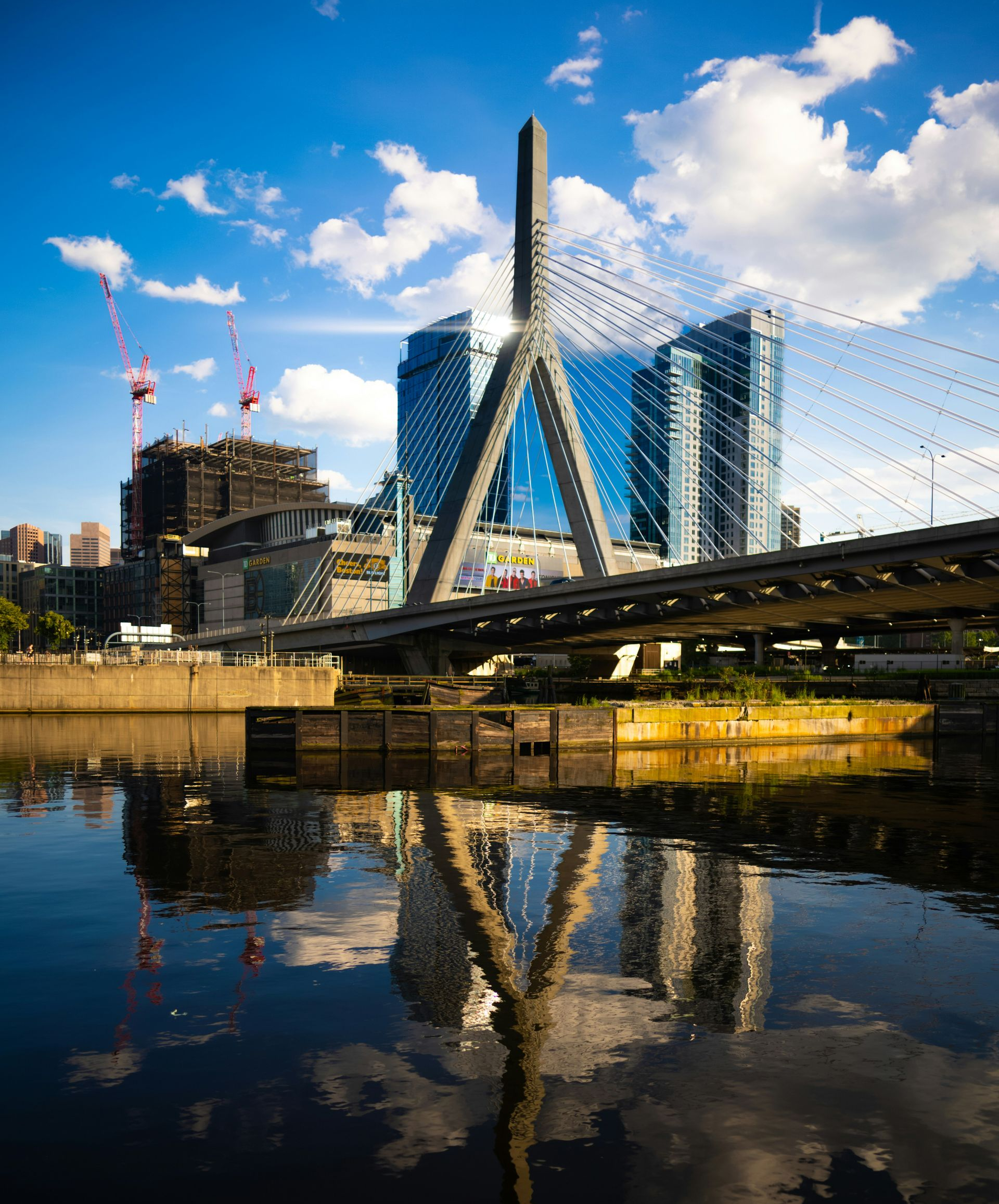 The Leonard P. Zakim Bunker Hill Memorial Bridge reflected in the Charles River under a blue sky with clouds.