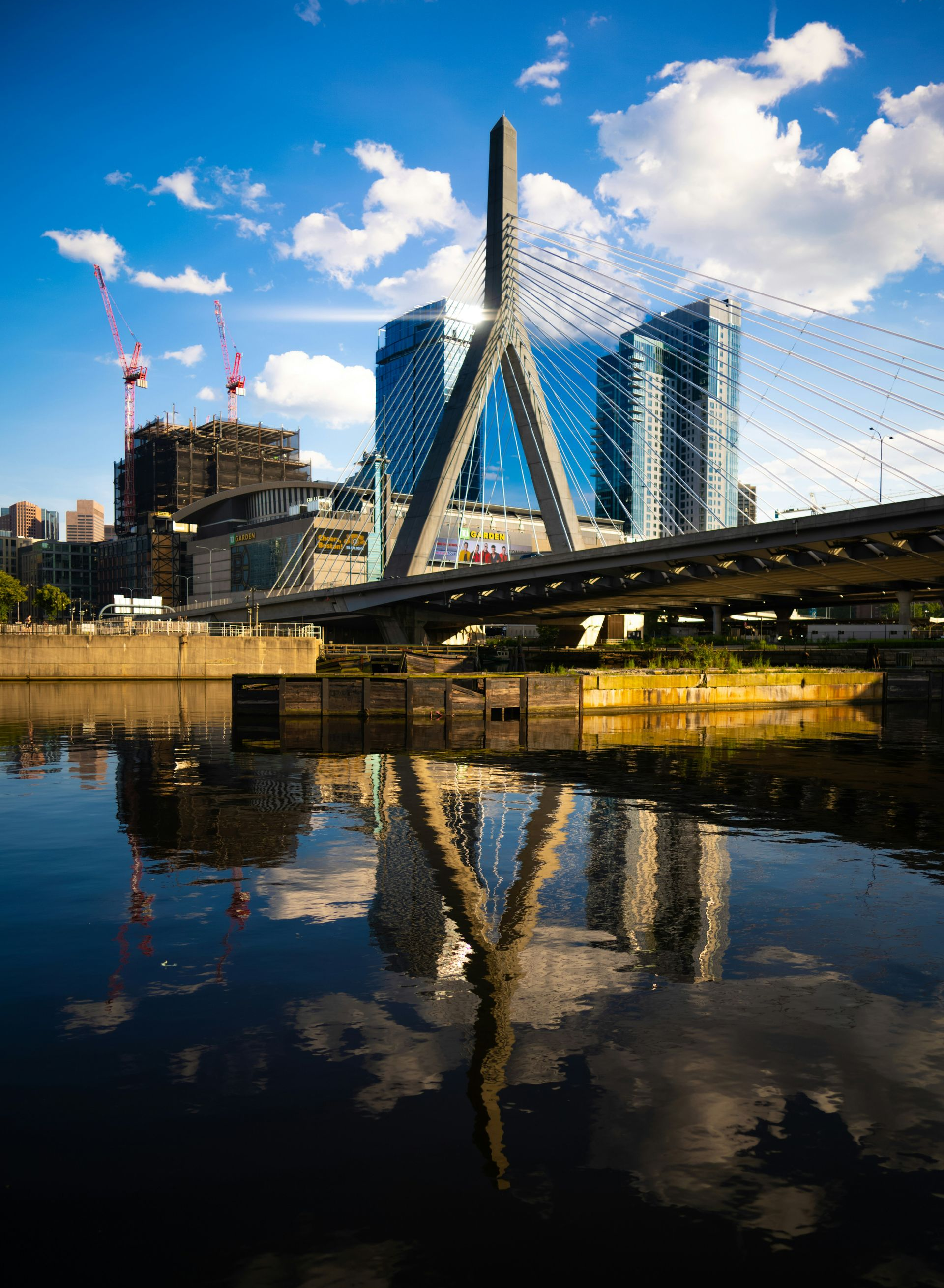 The Leonard P. Zakim Bunker Hill Memorial Bridge reflected in the Charles River under a blue sky with clouds.