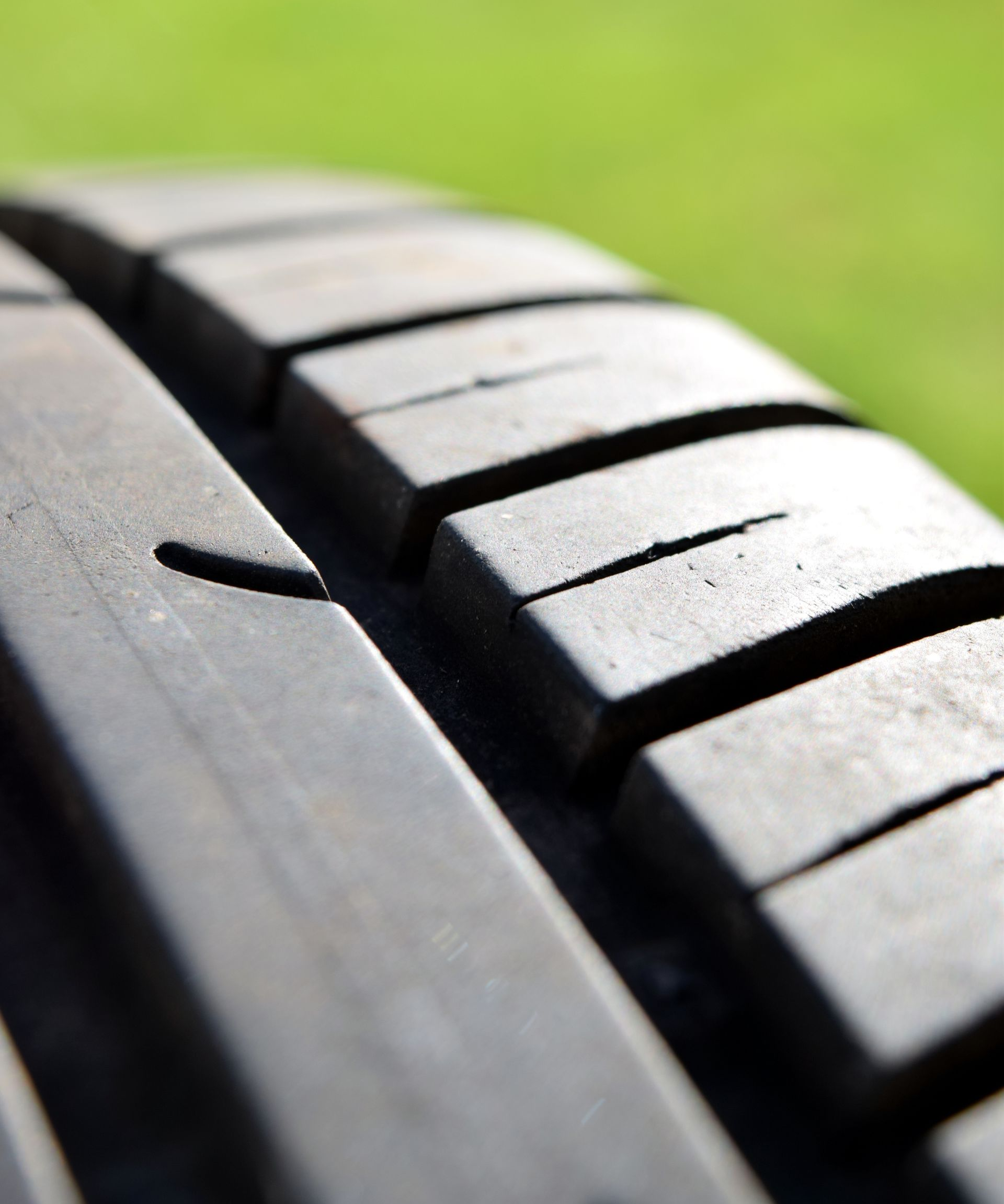 Close-up of a black tire tread with grooves, against a blurred green background