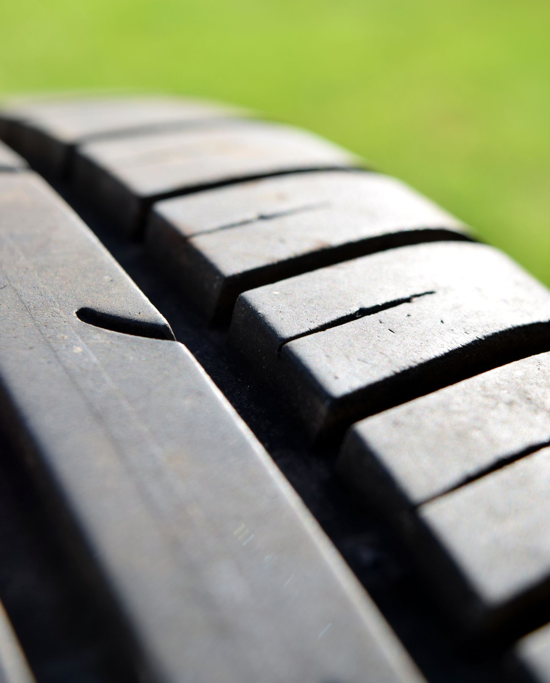 Close-up of a black tire tread with grooves, against a blurred green background