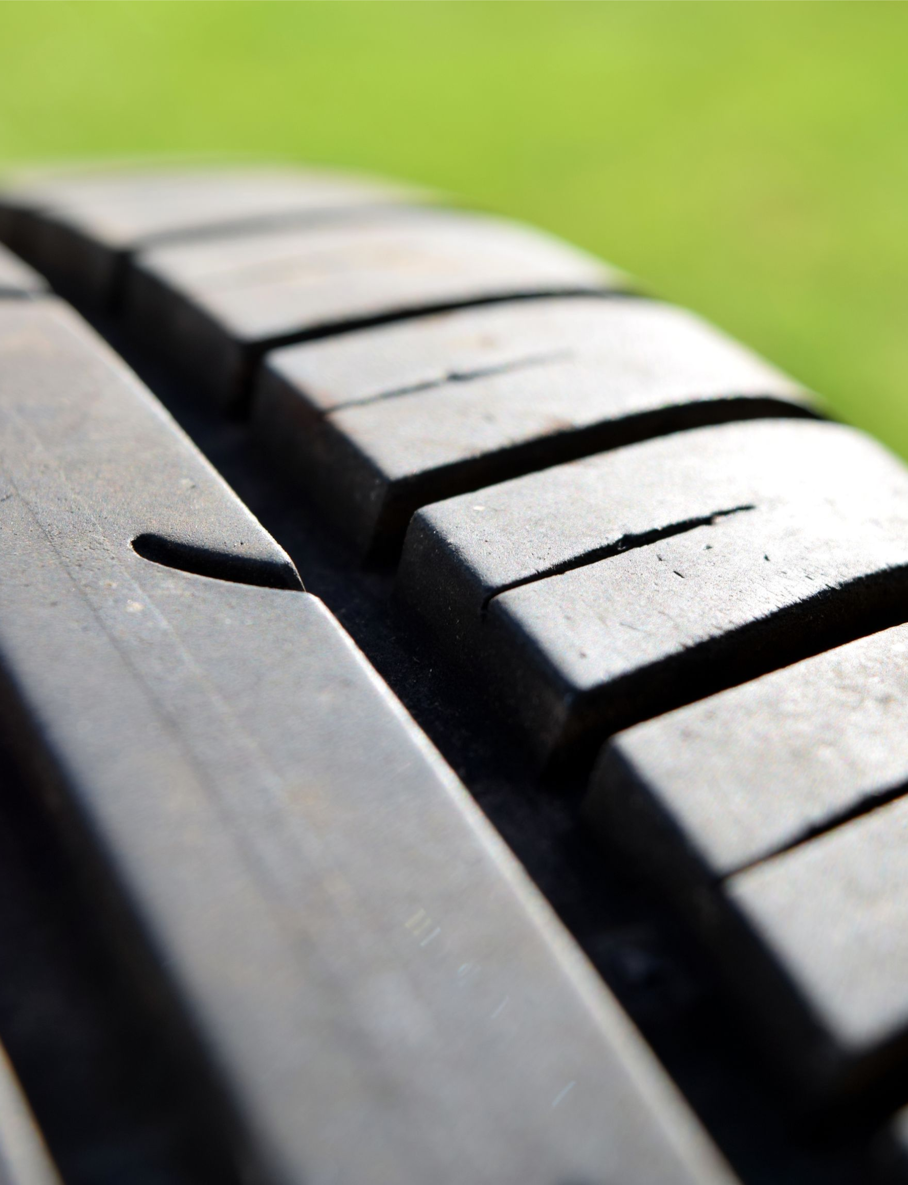 Close-up of a black tire tread with grooves, against a blurred green background