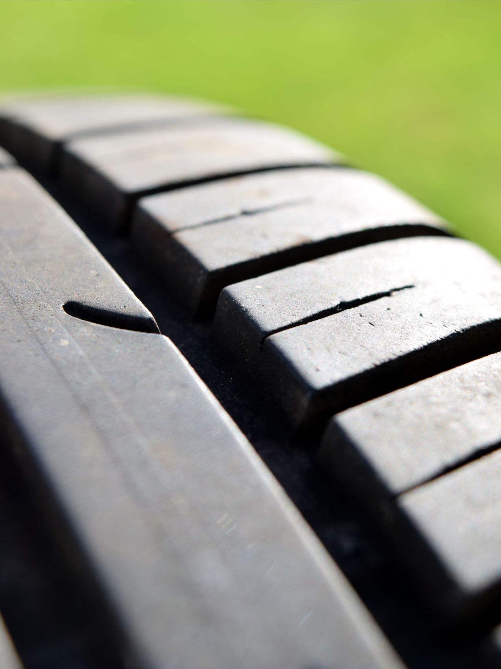 Close-up of a black tire tread with grooves, against a blurred green background