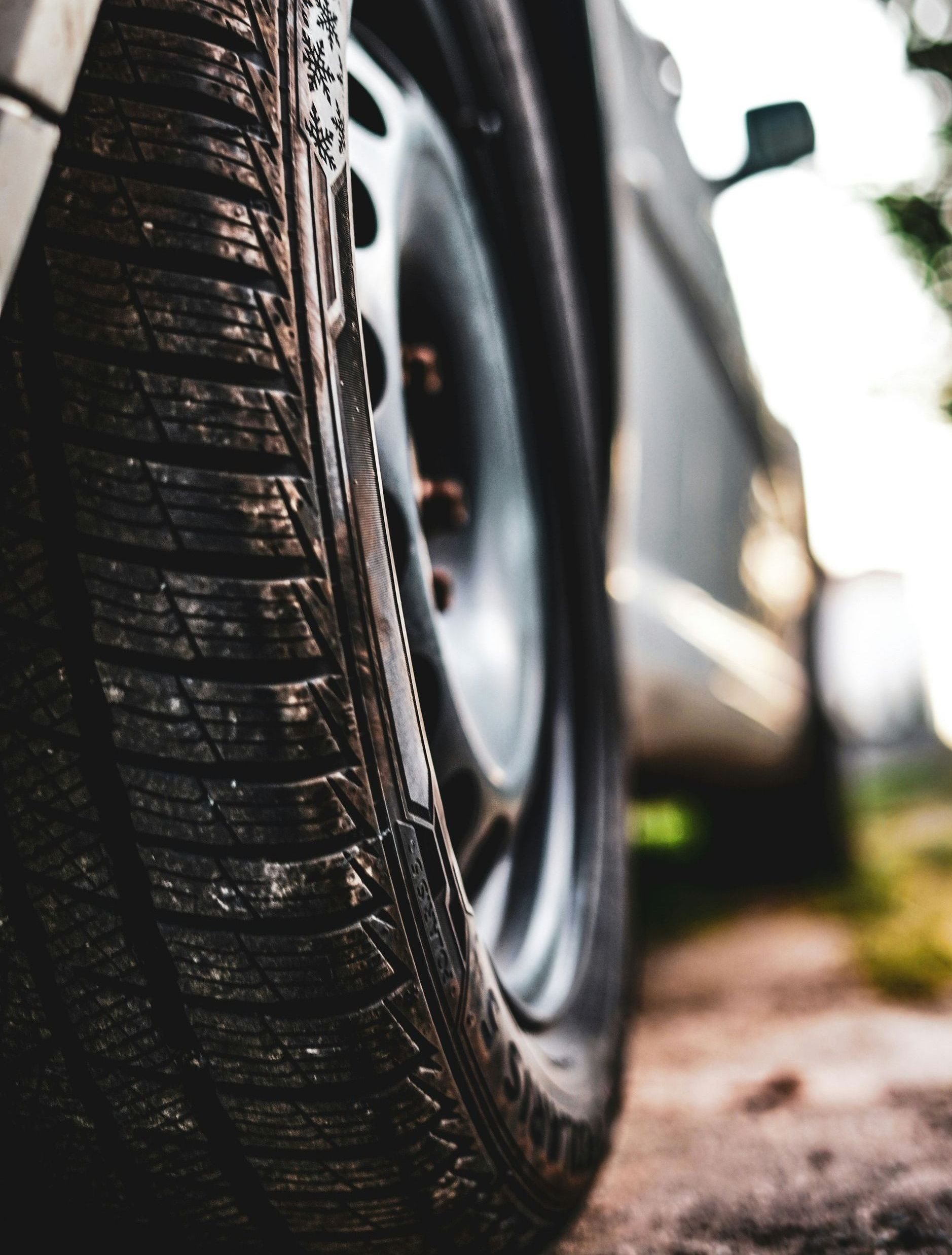 Close-up of a car tire on a dusty road, showing tread detail. Gray car body in background.