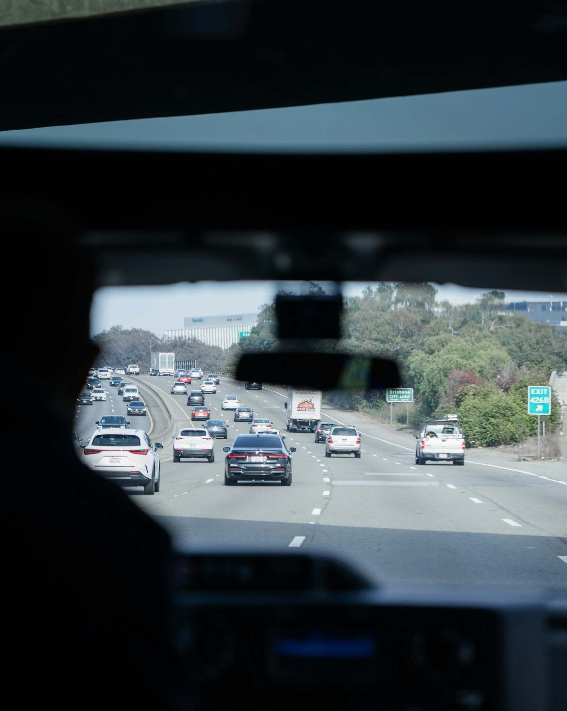 View from inside a car on a highway with multiple vehicles ahead and greenery along the road