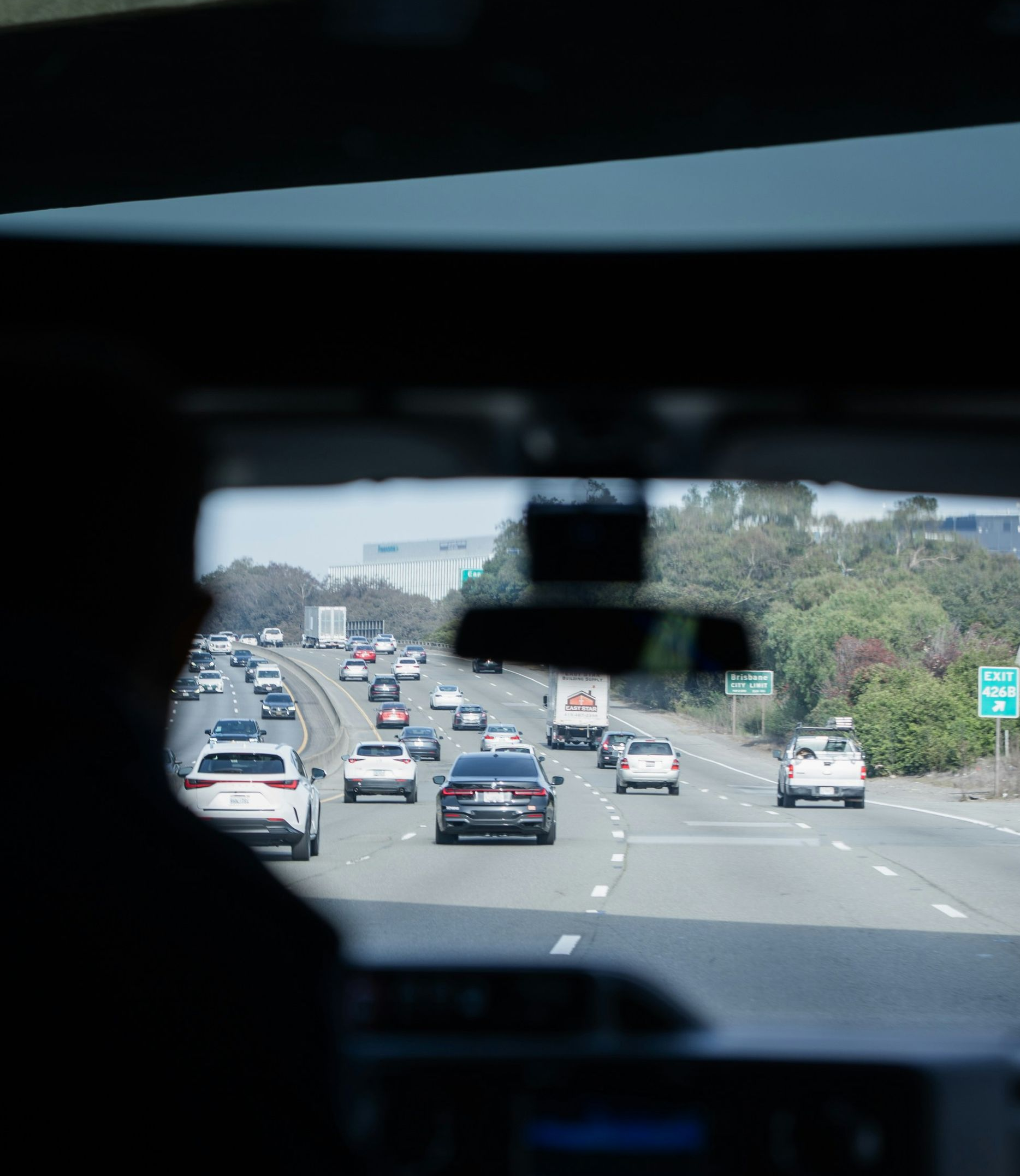 View from inside a car on a highway with multiple vehicles ahead and greenery along the road