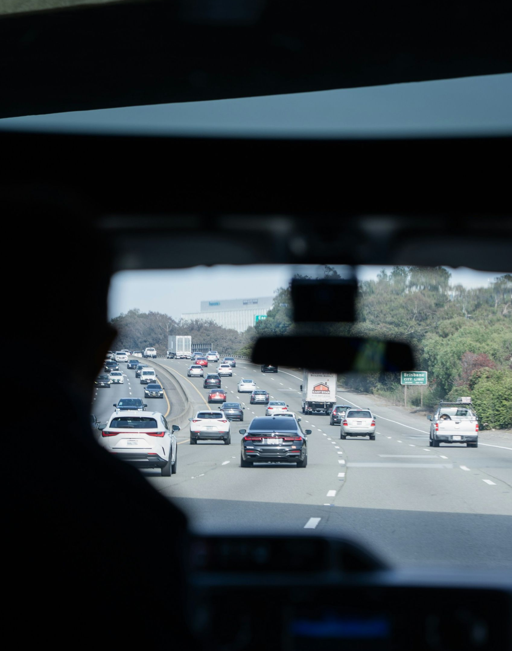 View from inside a car on a highway with multiple vehicles ahead and greenery along the road