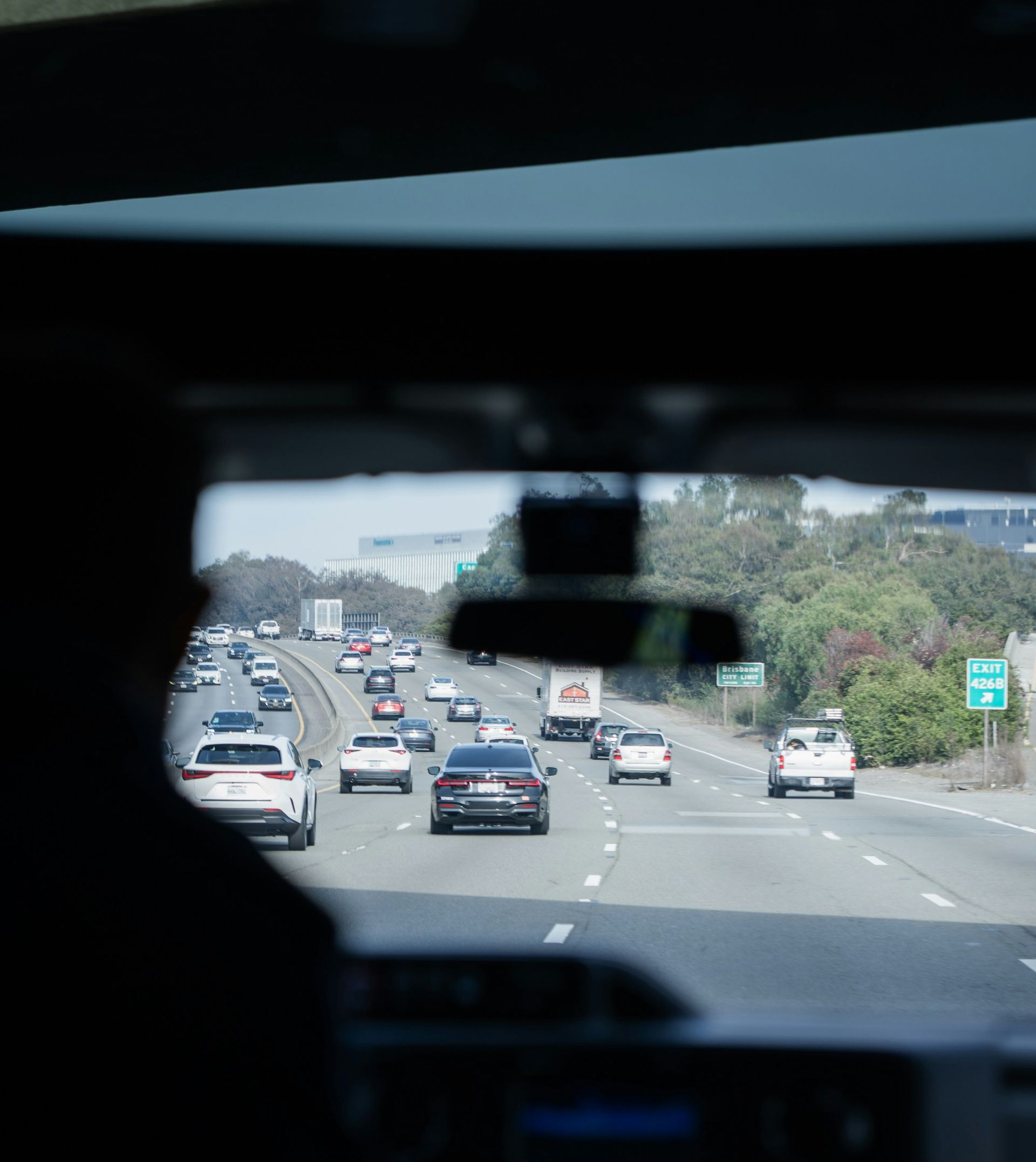 View from inside a car on a highway with multiple vehicles ahead and greenery along the road