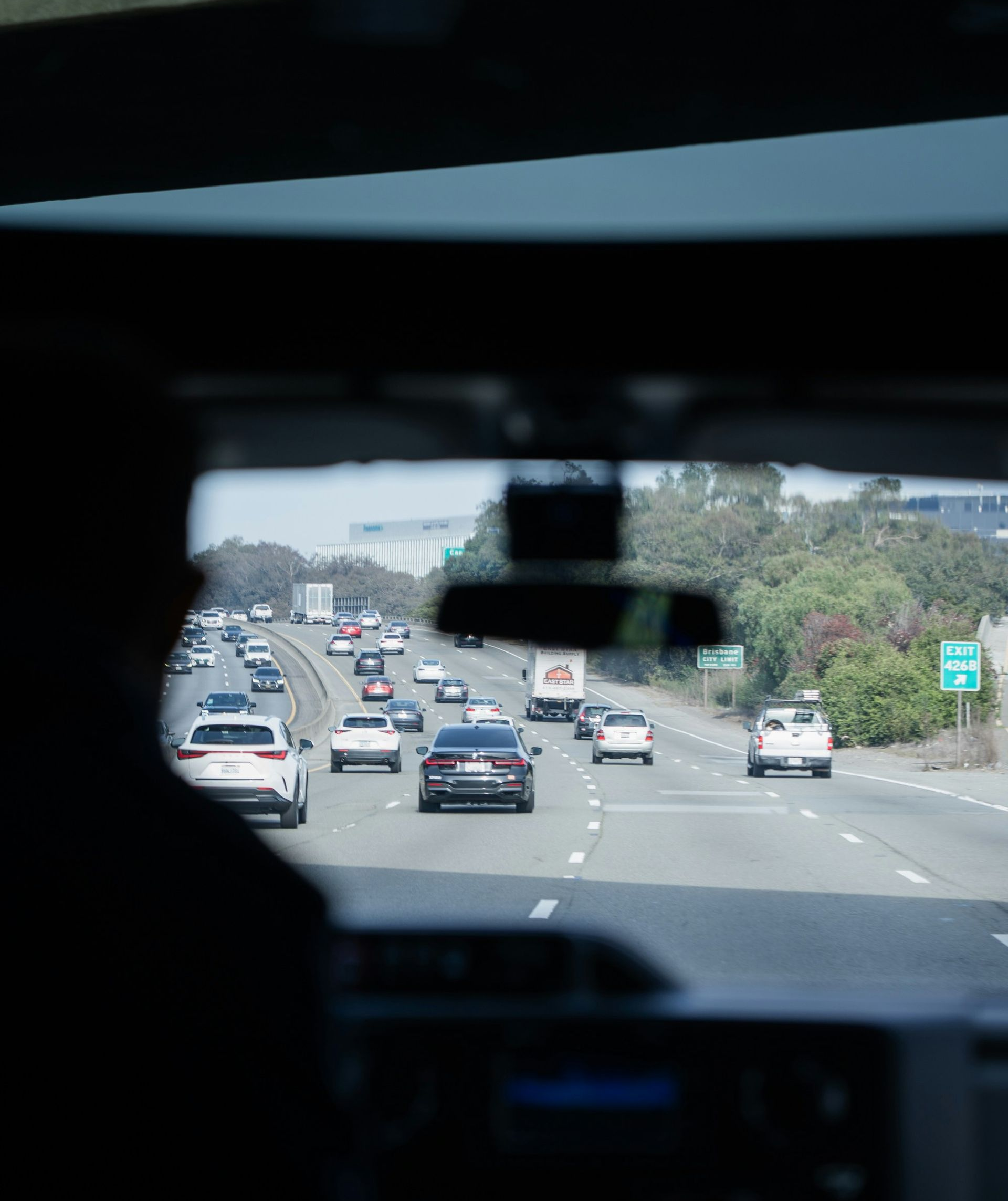 View from inside a car on a highway with multiple vehicles ahead and greenery along the road