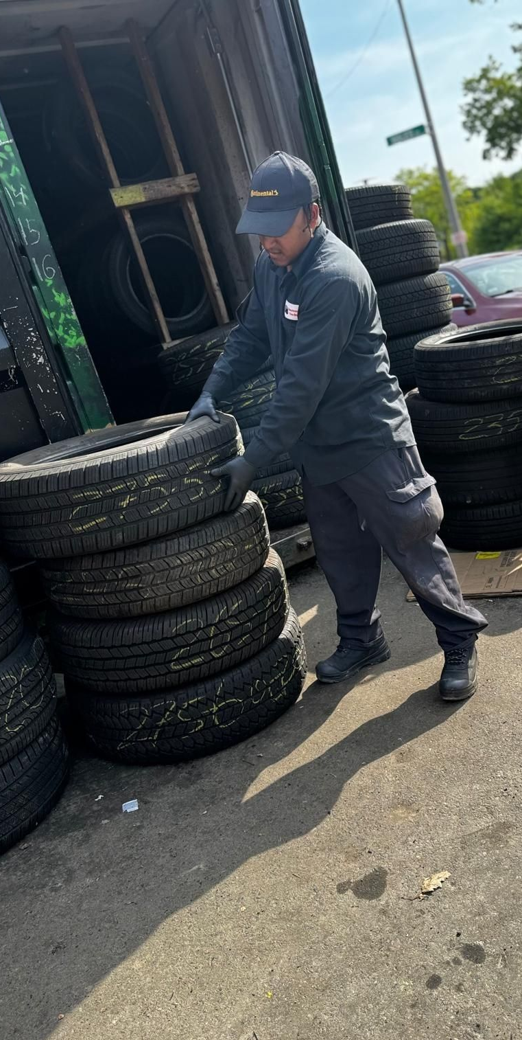 Worker stacking tires beside a red cart outside a building on a sunny day