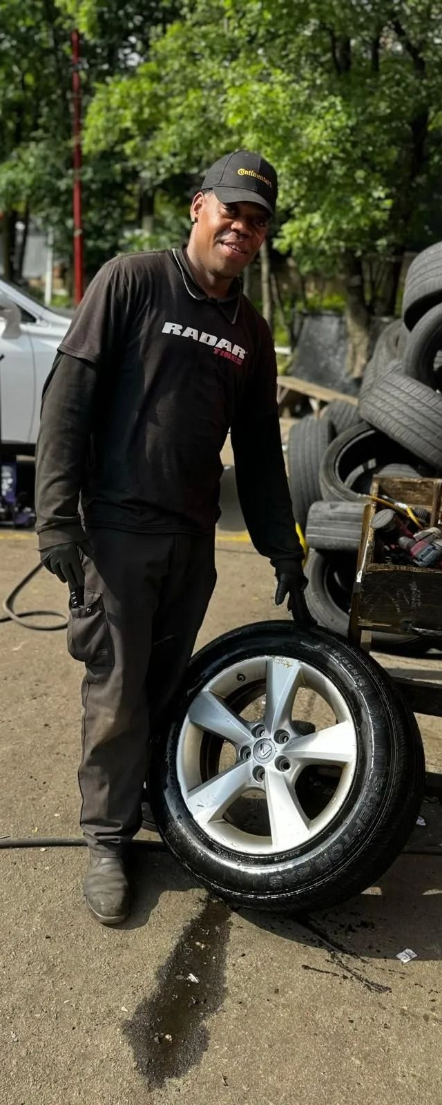 Mechanic points at a car tire in a shop. Tires stacked nearby.