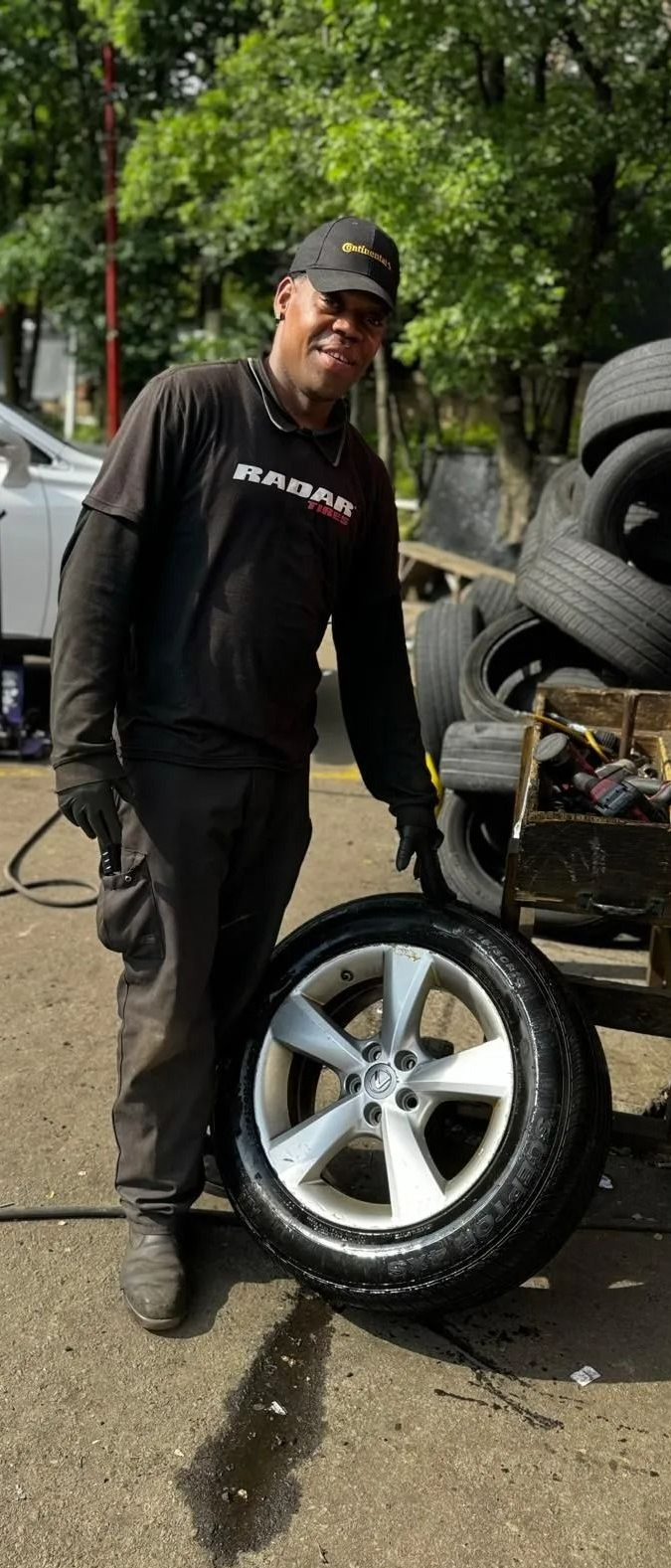 Mechanic points at a car tire in a shop. Tires stacked nearby.