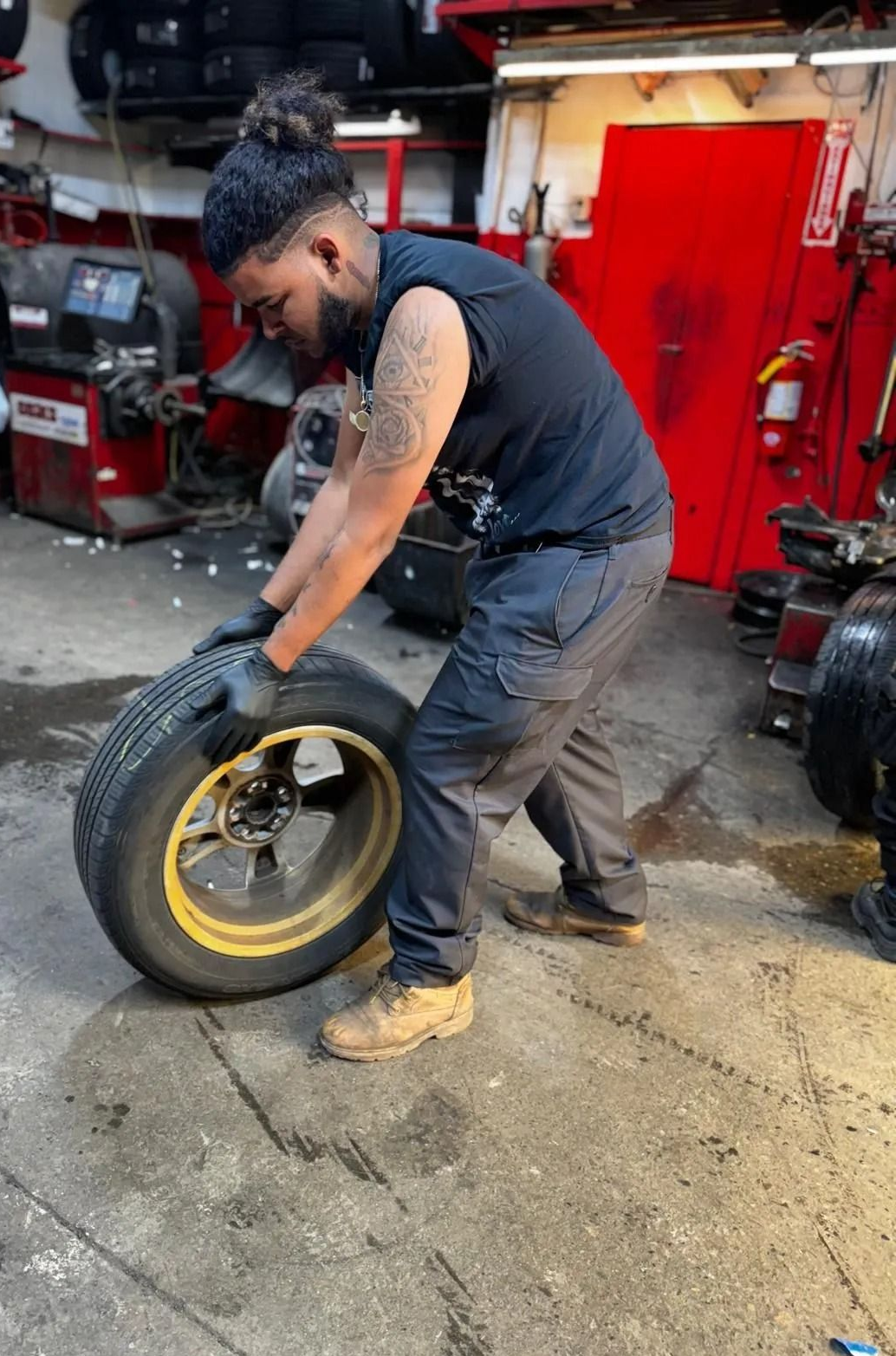 Man in garage, lifting a tire with yellow rim.