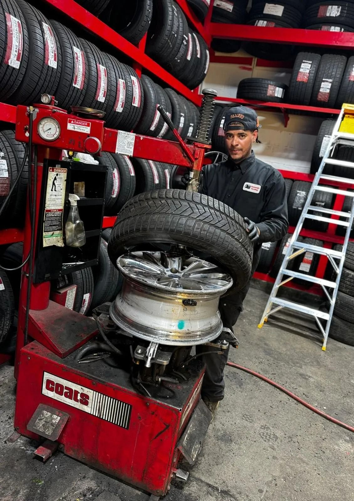 Mechanic using tire changer on a car wheel in a tire shop with stacked tires and tools nearby