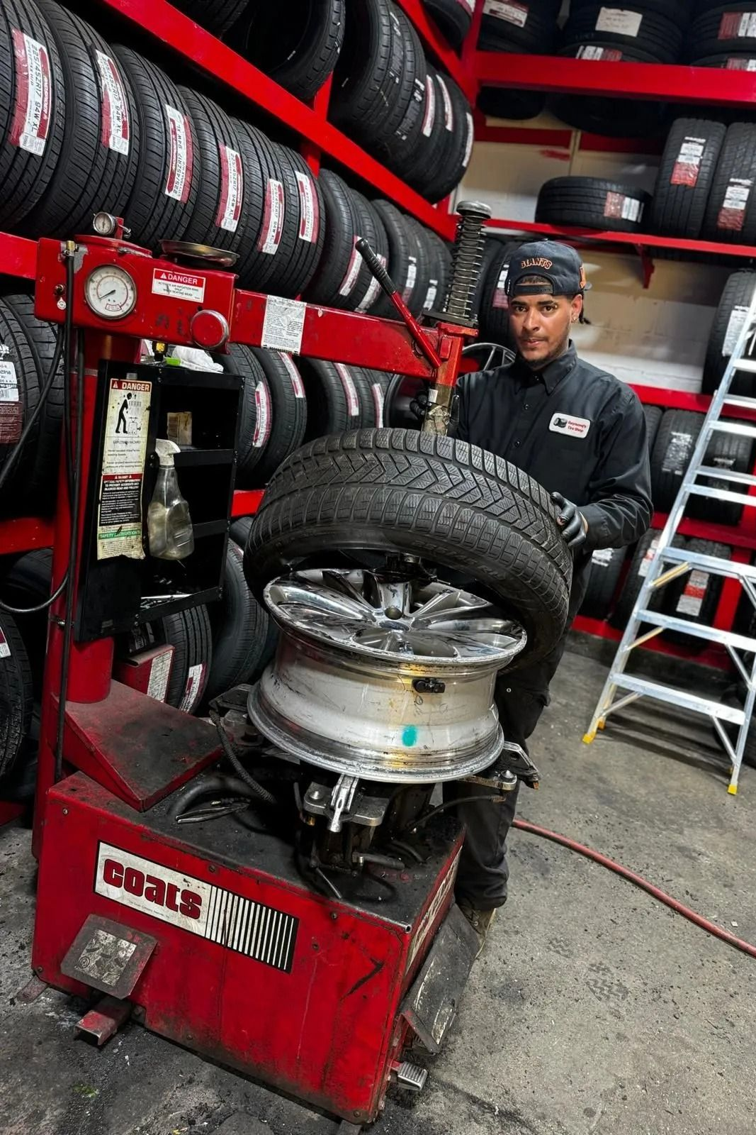 Mechanic using tire changer on a car wheel in a tire shop with stacked tires and tools nearby