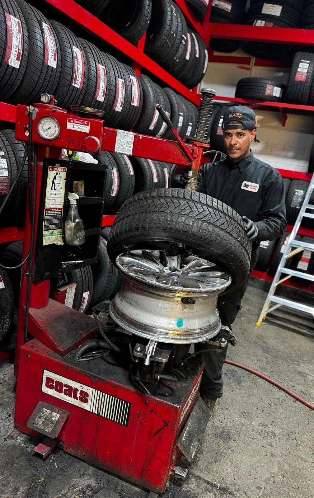 Mechanic using tire changer on a car wheel in a tire shop with stacked tires and tools nearby