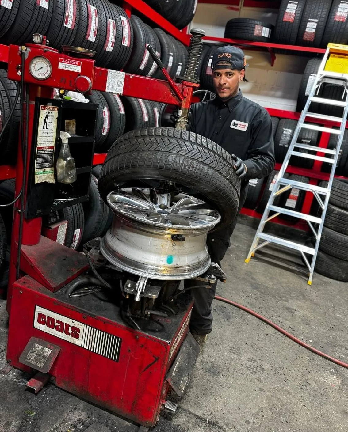 Mechanic using tire changer on a car wheel in a tire shop with stacked tires and tools nearby