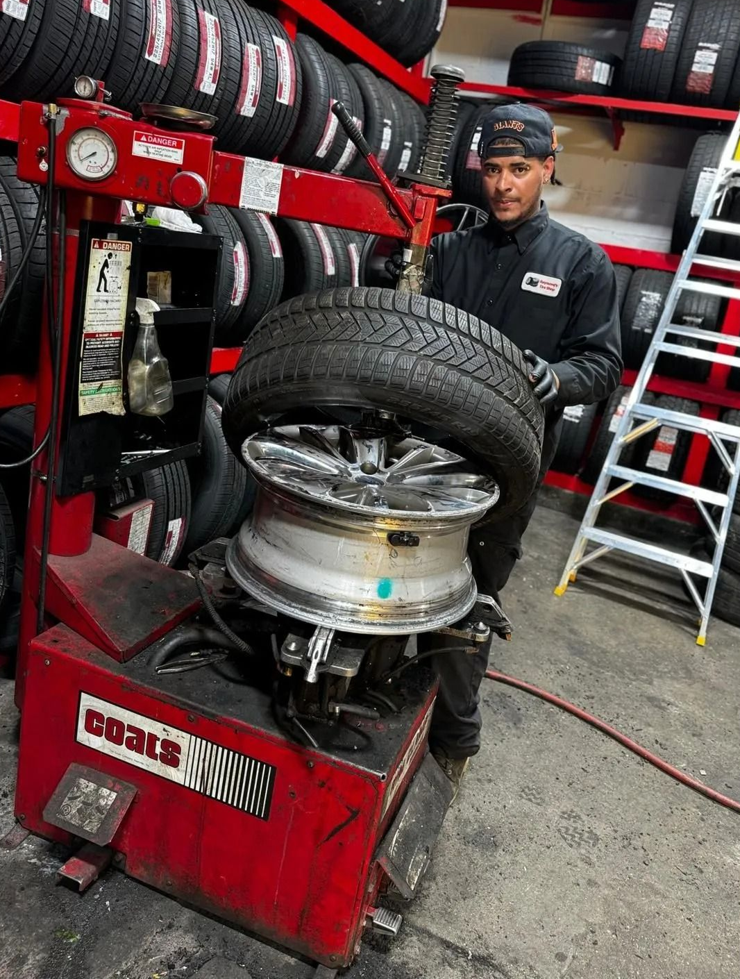 Mechanic using tire changer on a car wheel in a tire shop with stacked tires and tools nearby