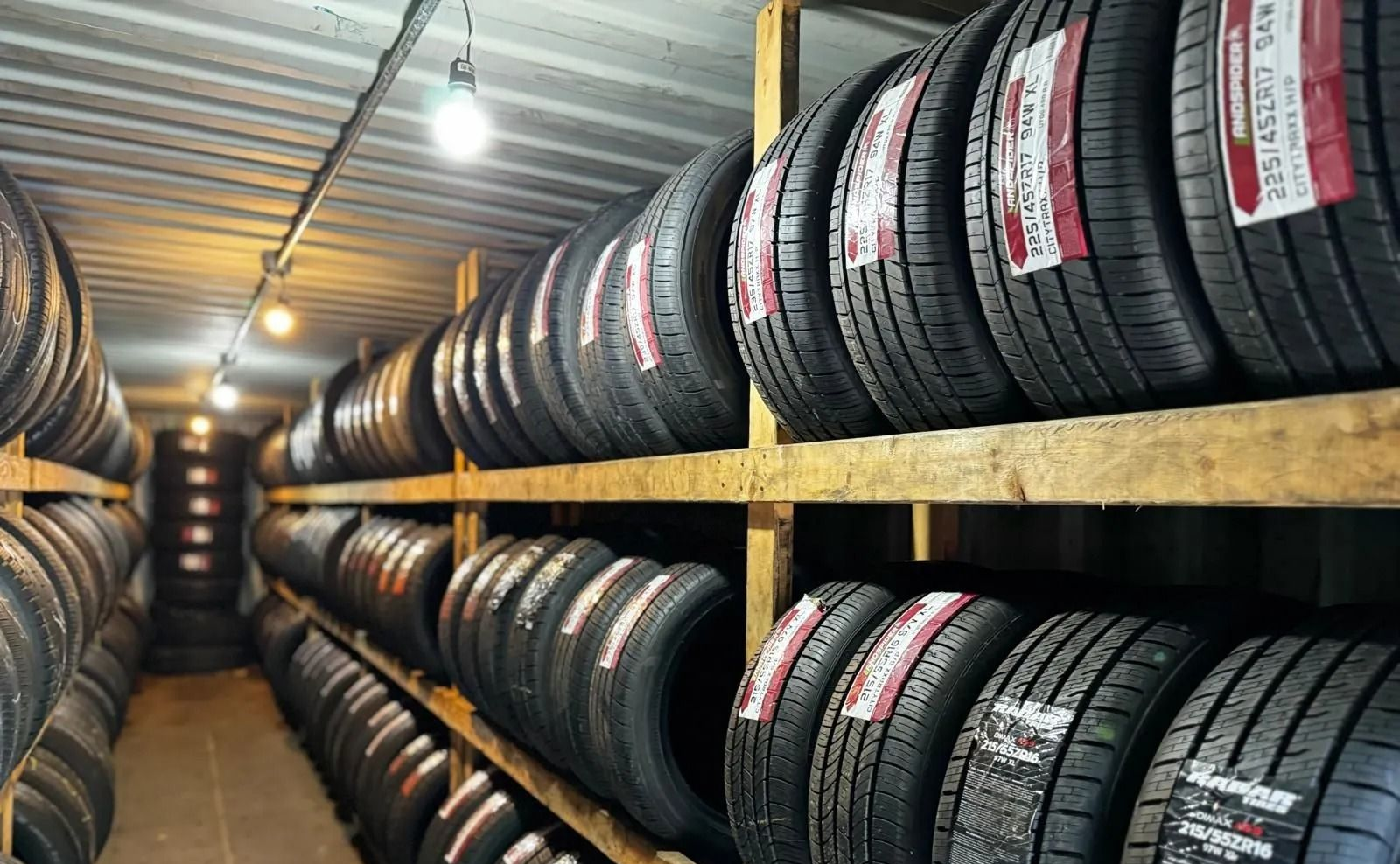 Rows of stacked tires on wooden shelves in a narrow warehouse aisle