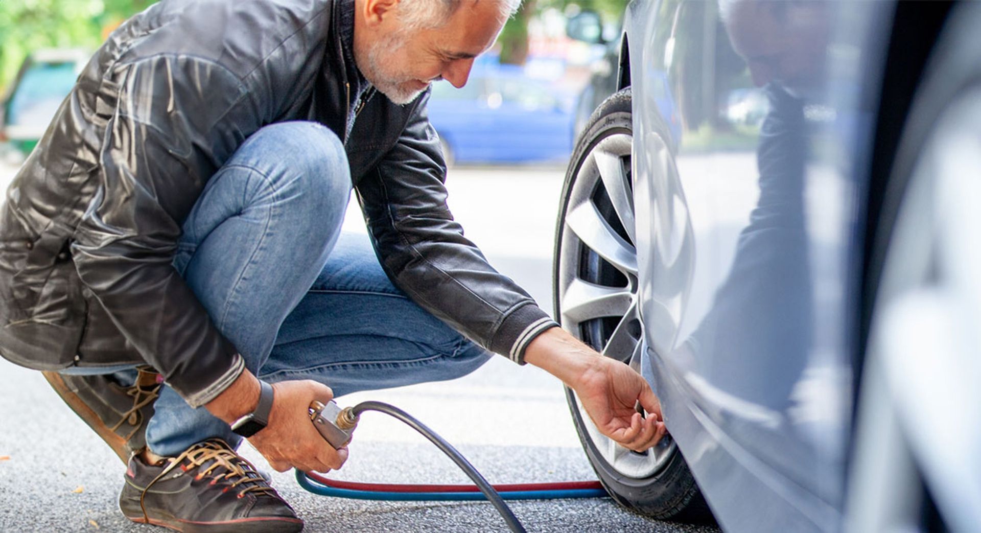 Man crouching beside a car, using a portable air compressor to inflate a tire.