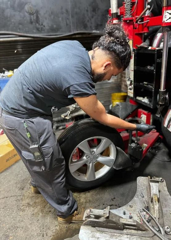 Mechanic changing a tire using a machine in a garage. The person is wearing gray pants and a blue shirt.
