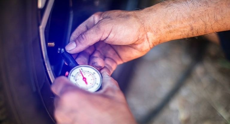 Hands using a pressure gauge to check a bicycle tire valve under blue lighting