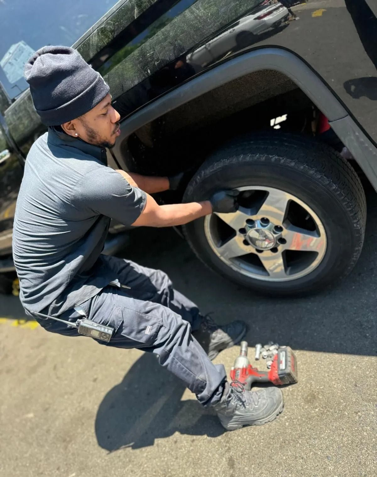 A person in dark clothing changes a tire on a black vehicle, with tools nearby.