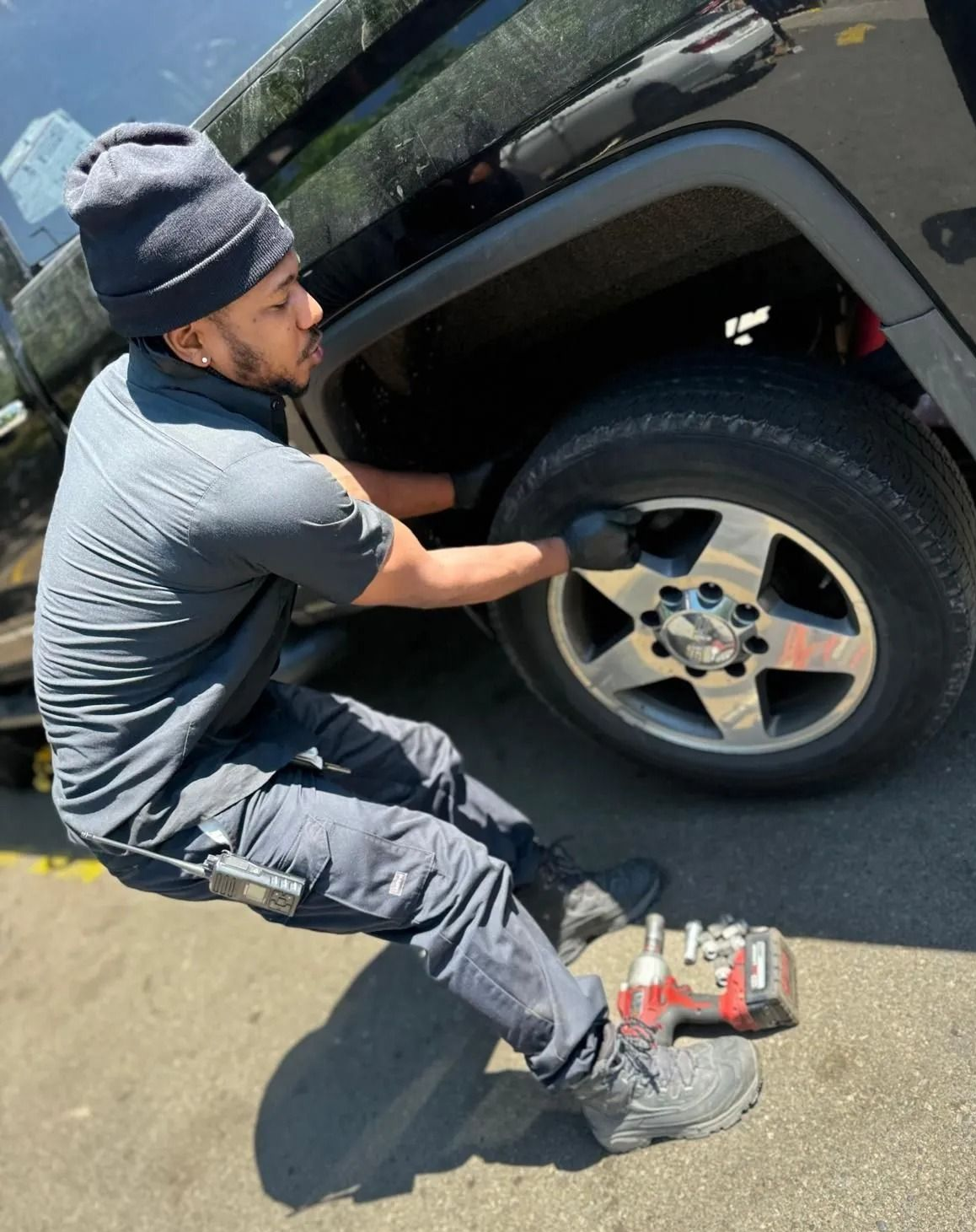 A person in dark clothing changes a tire on a black vehicle, with tools nearby.